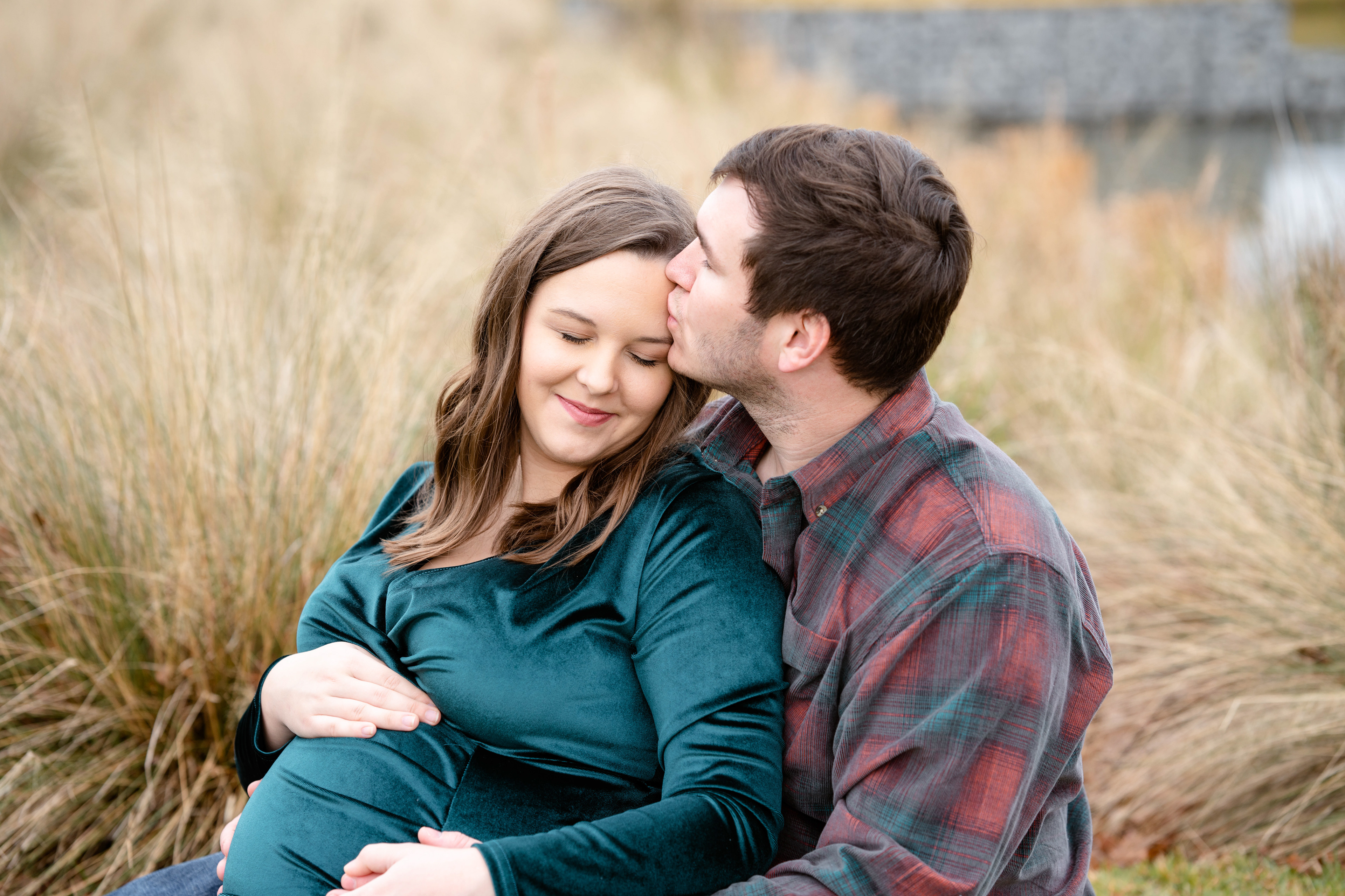 Husband kisses his wife while sitting for a maternity photo