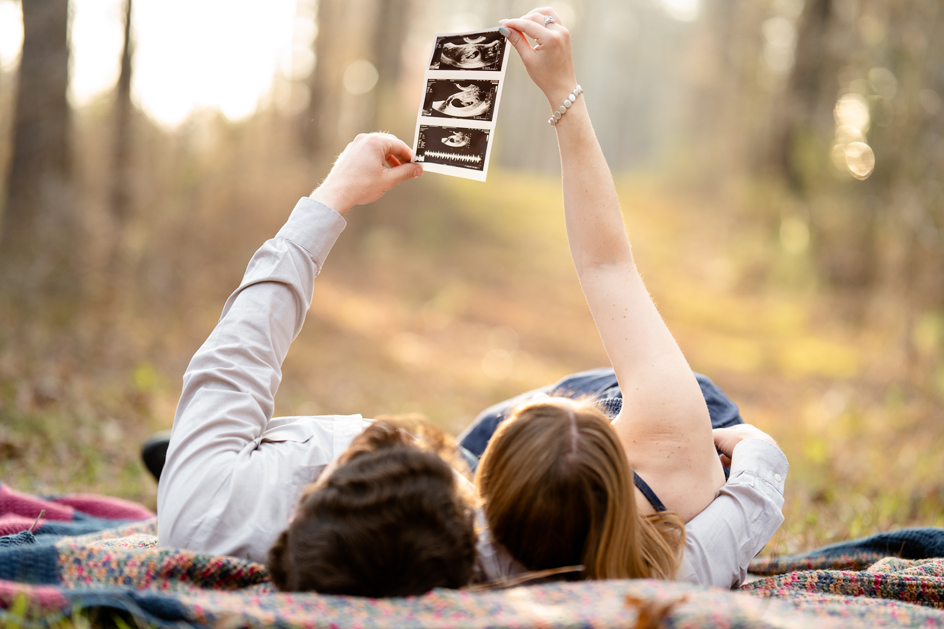 Couple looking up at sonogram while laying on a blanket in the woods