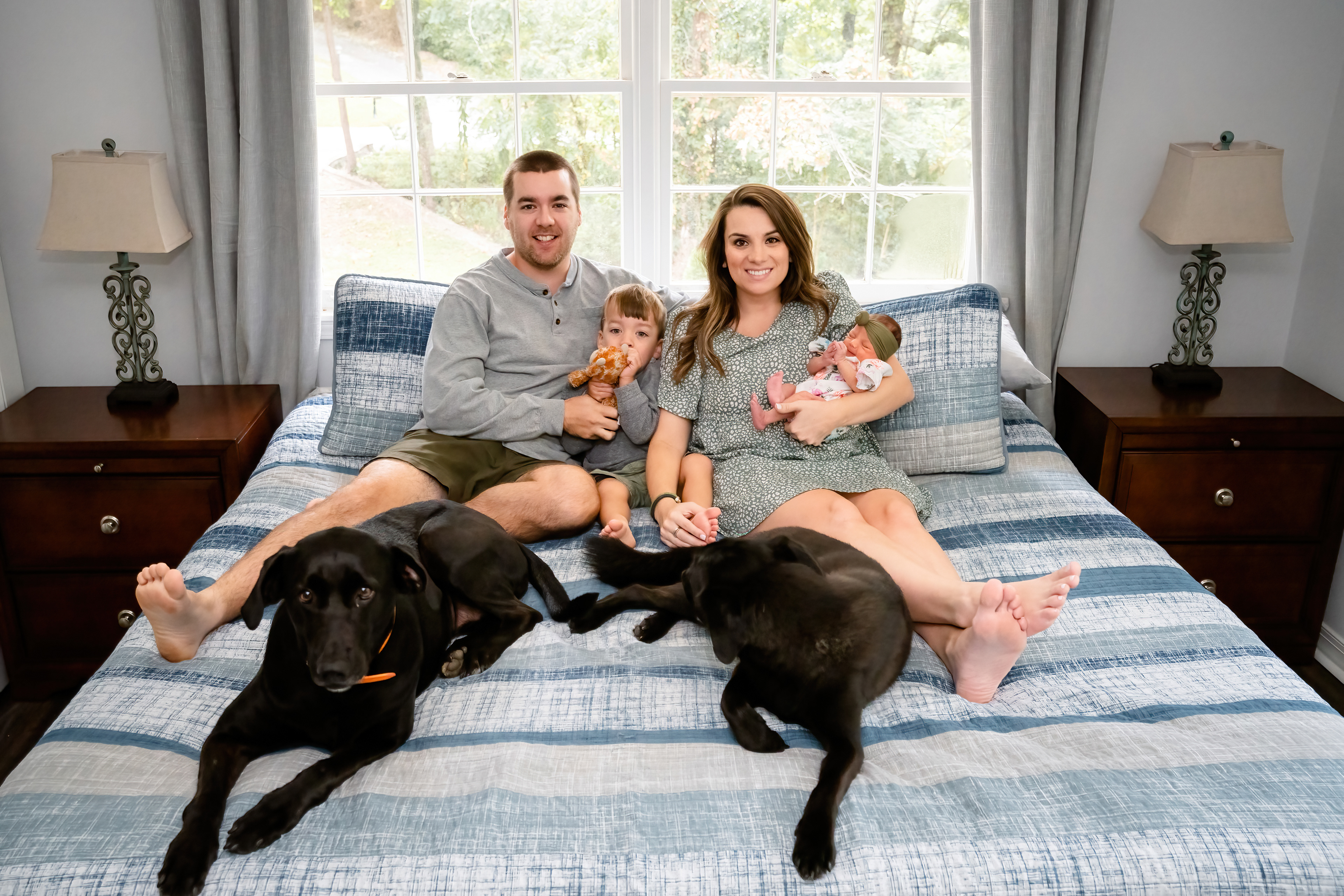 Family with their newborn and dogs on bed in the comfort of their home