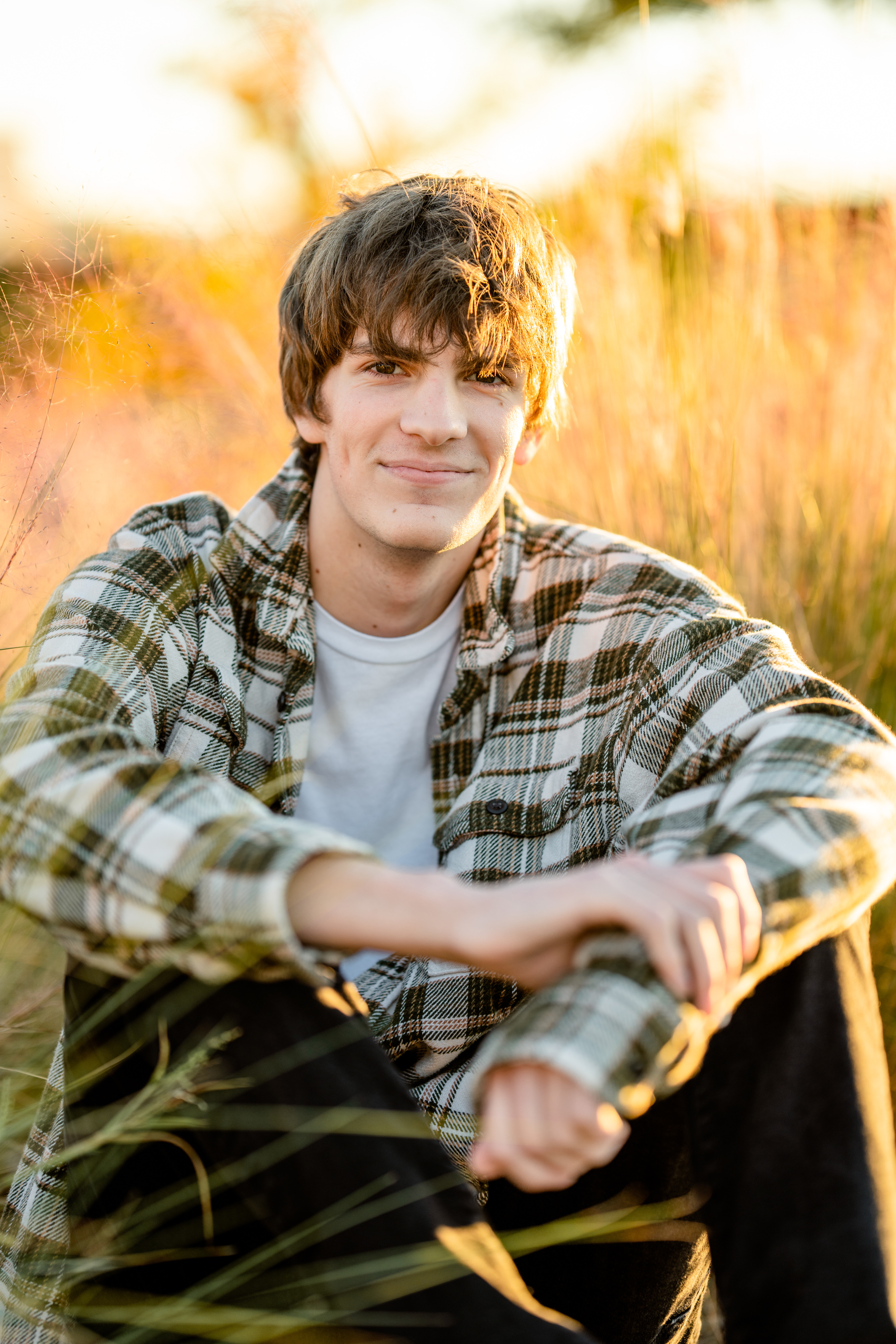 Senior boy sits in tall grass at sunset