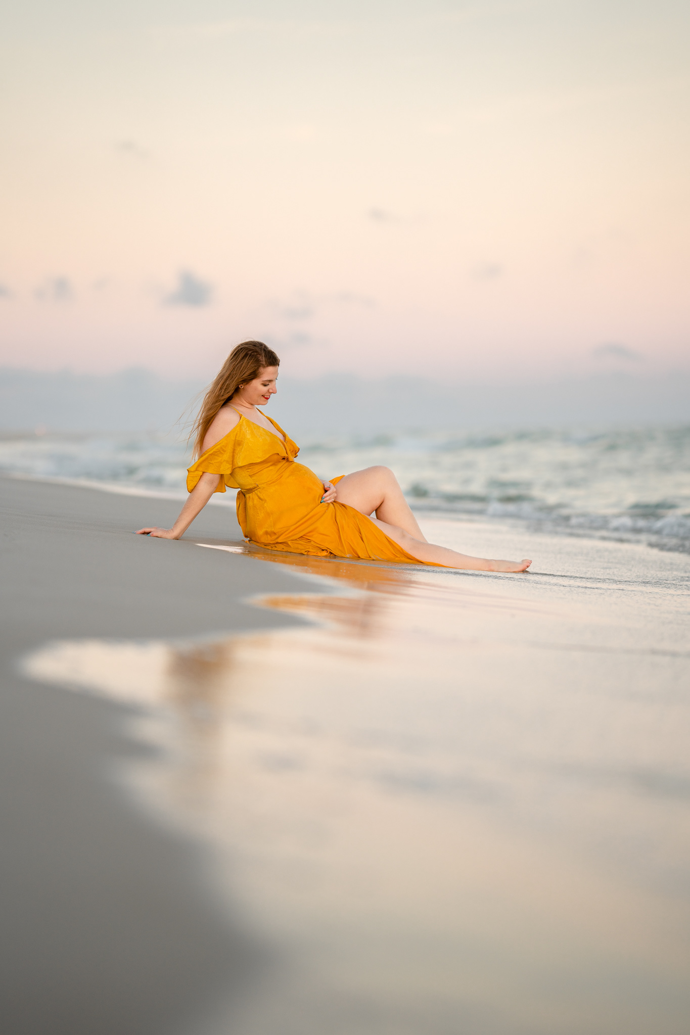 Pregnant woman caresses her belly on the sand at the beach