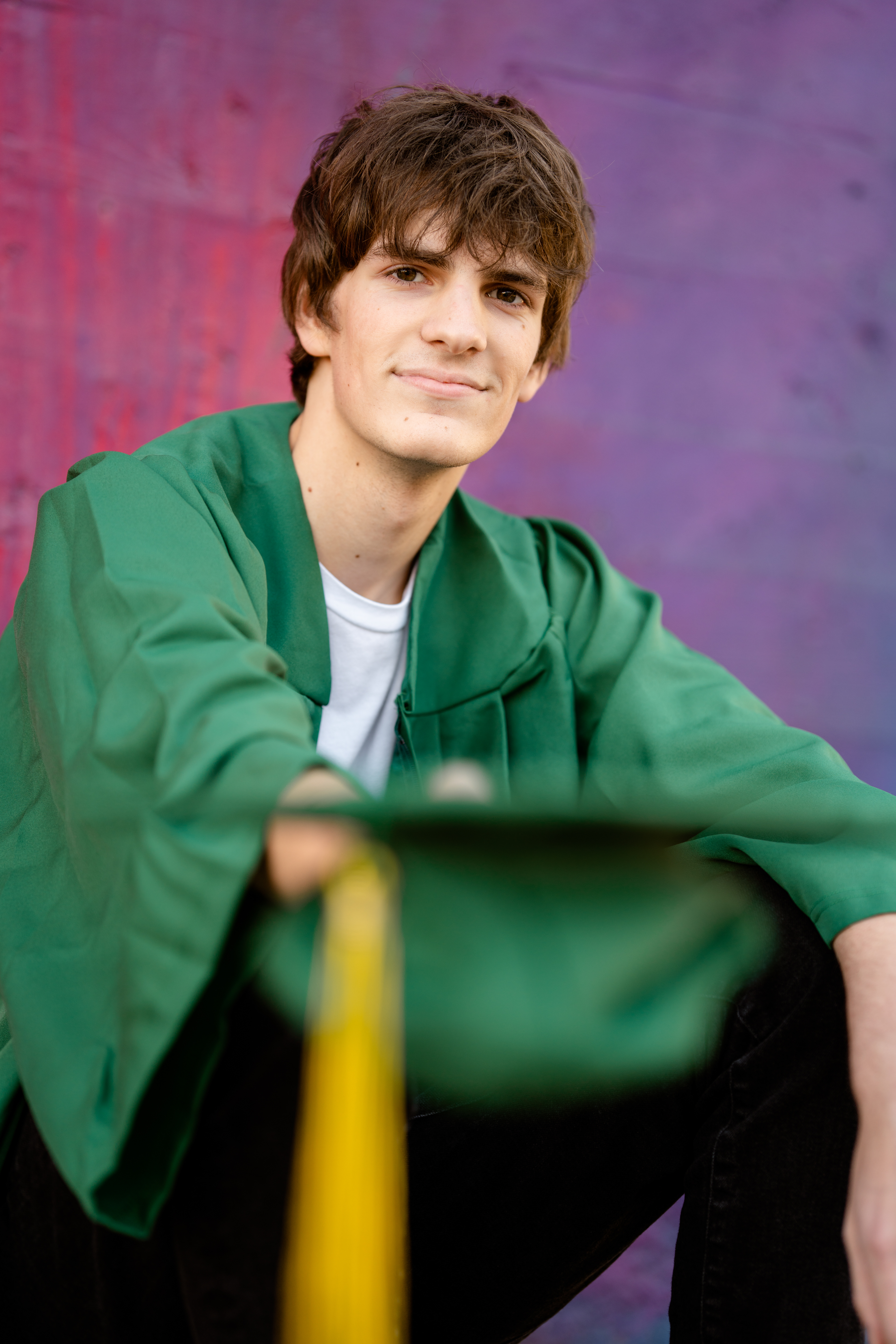 Senior boy holds graduation cap out to camera
