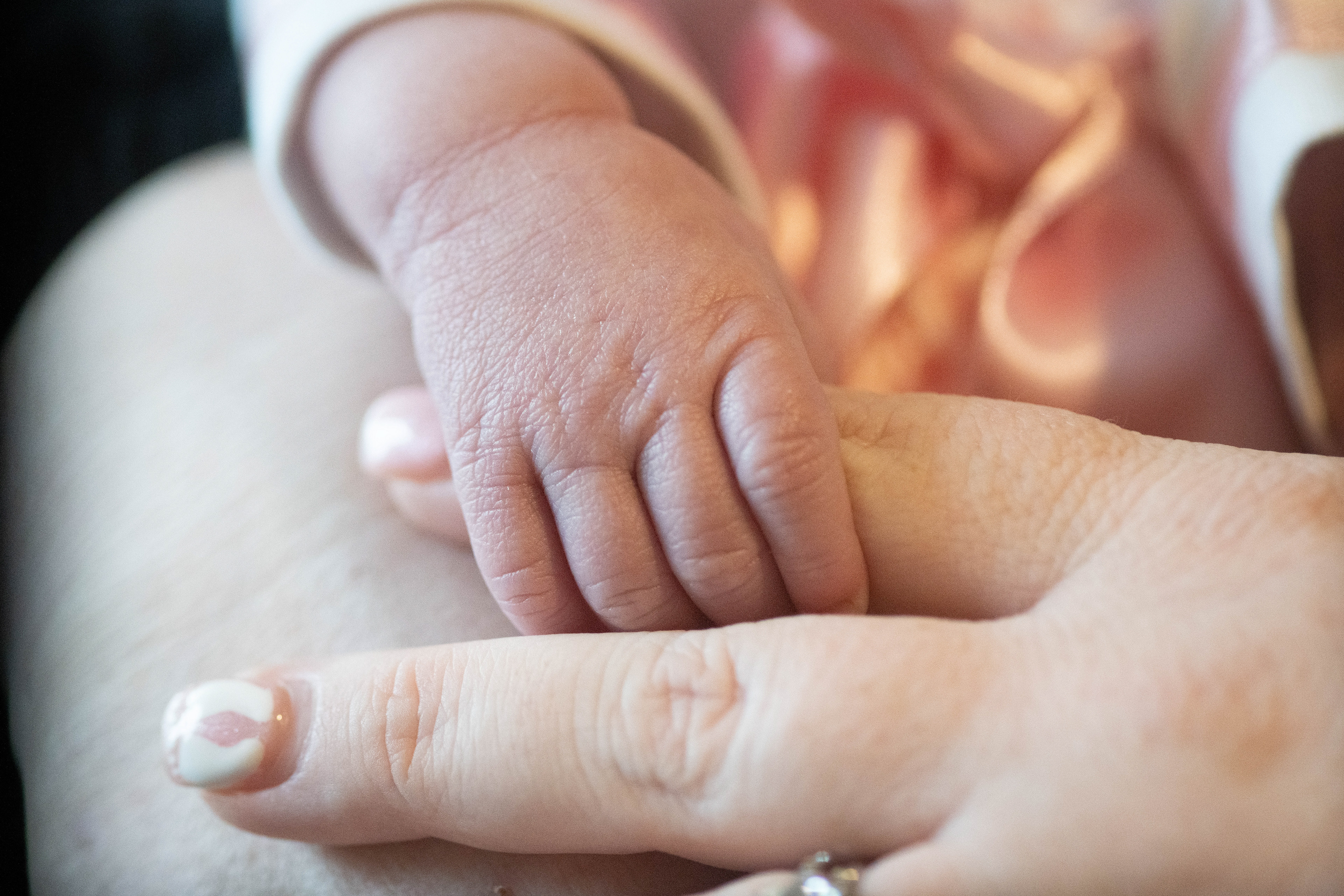 Detail shot of newborn holding her mommy's finger