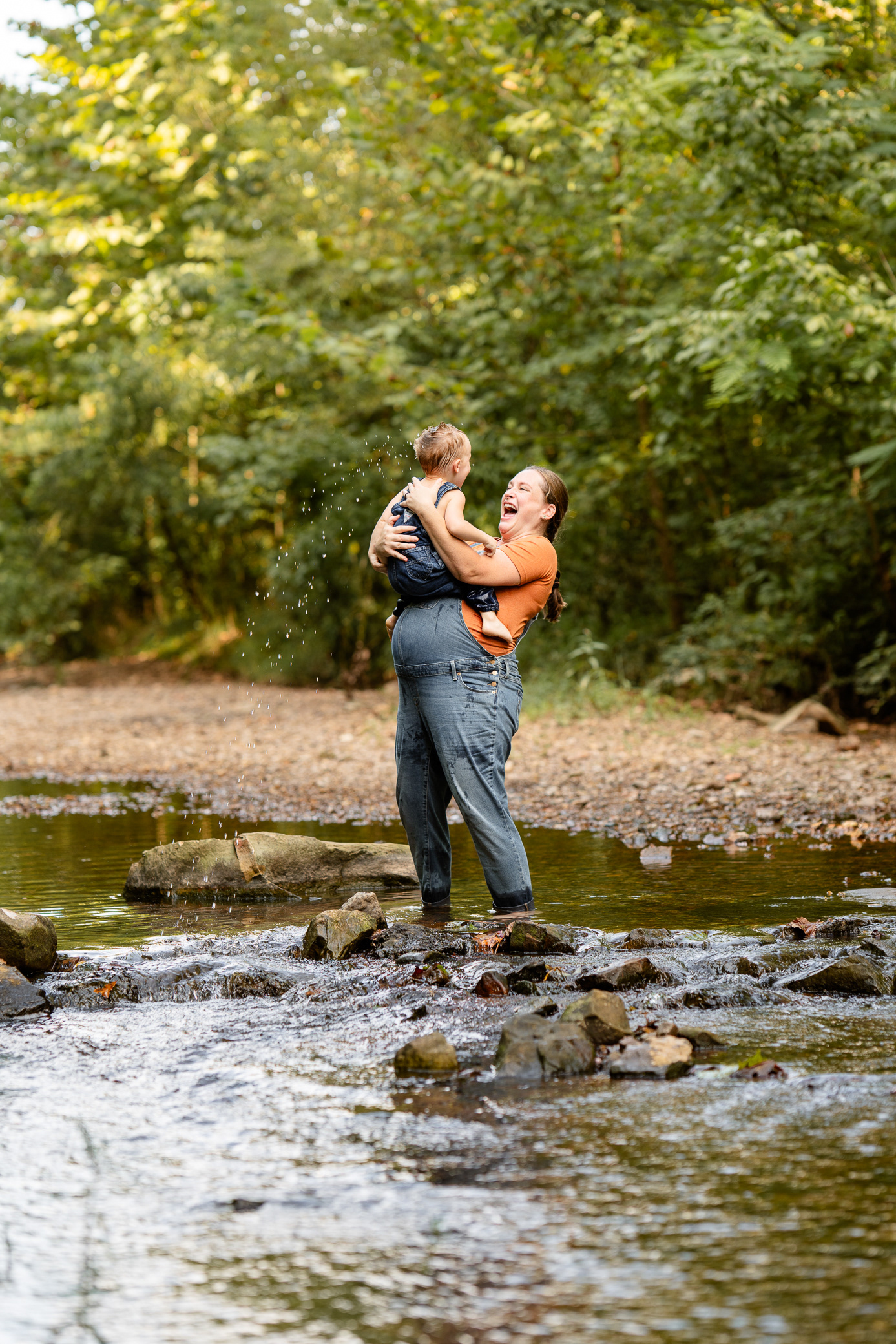 Mother dips son's head in the water at creek maternity session