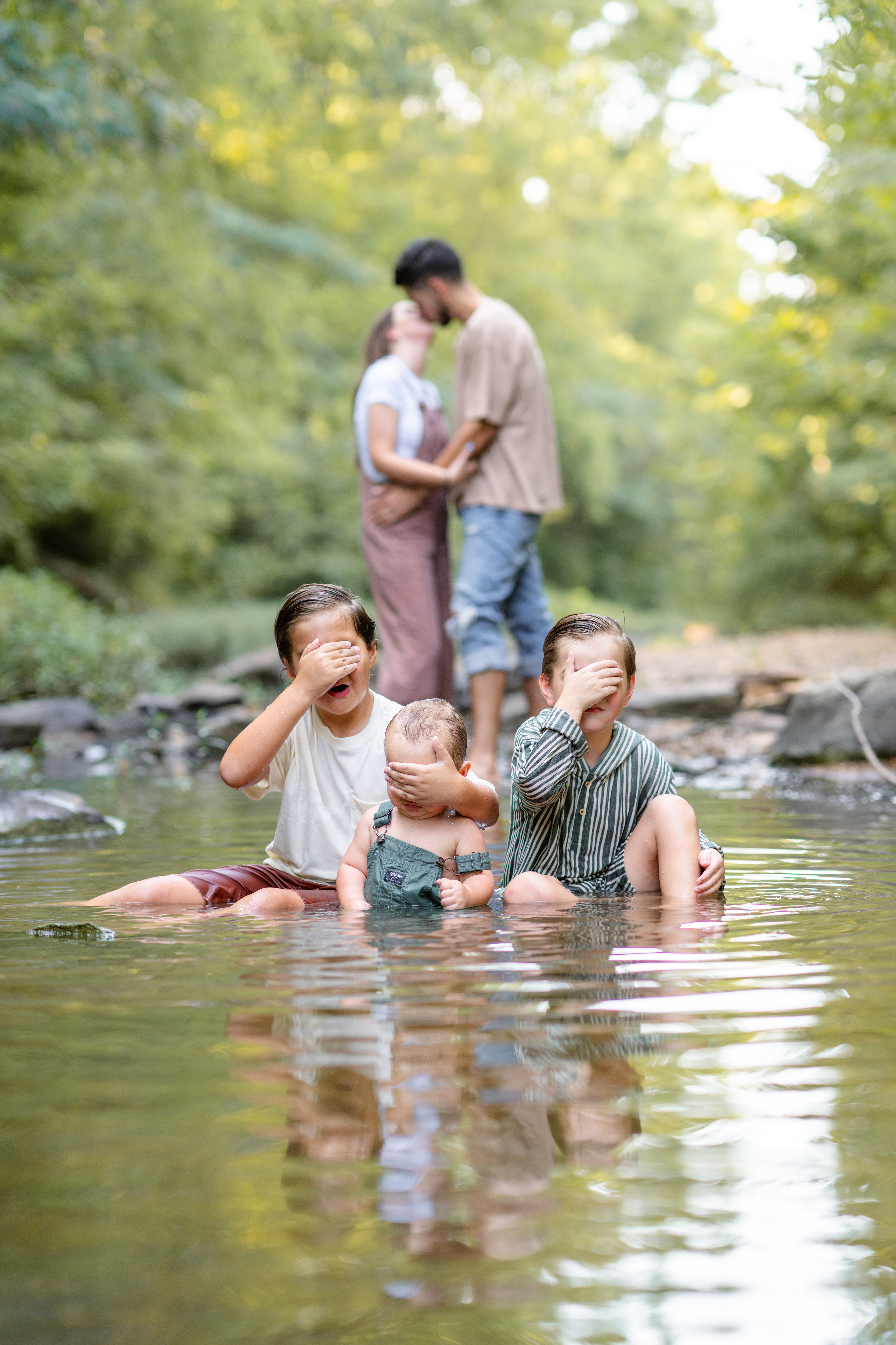 3 brothers cover their eyes while mom and dad kiss in the background