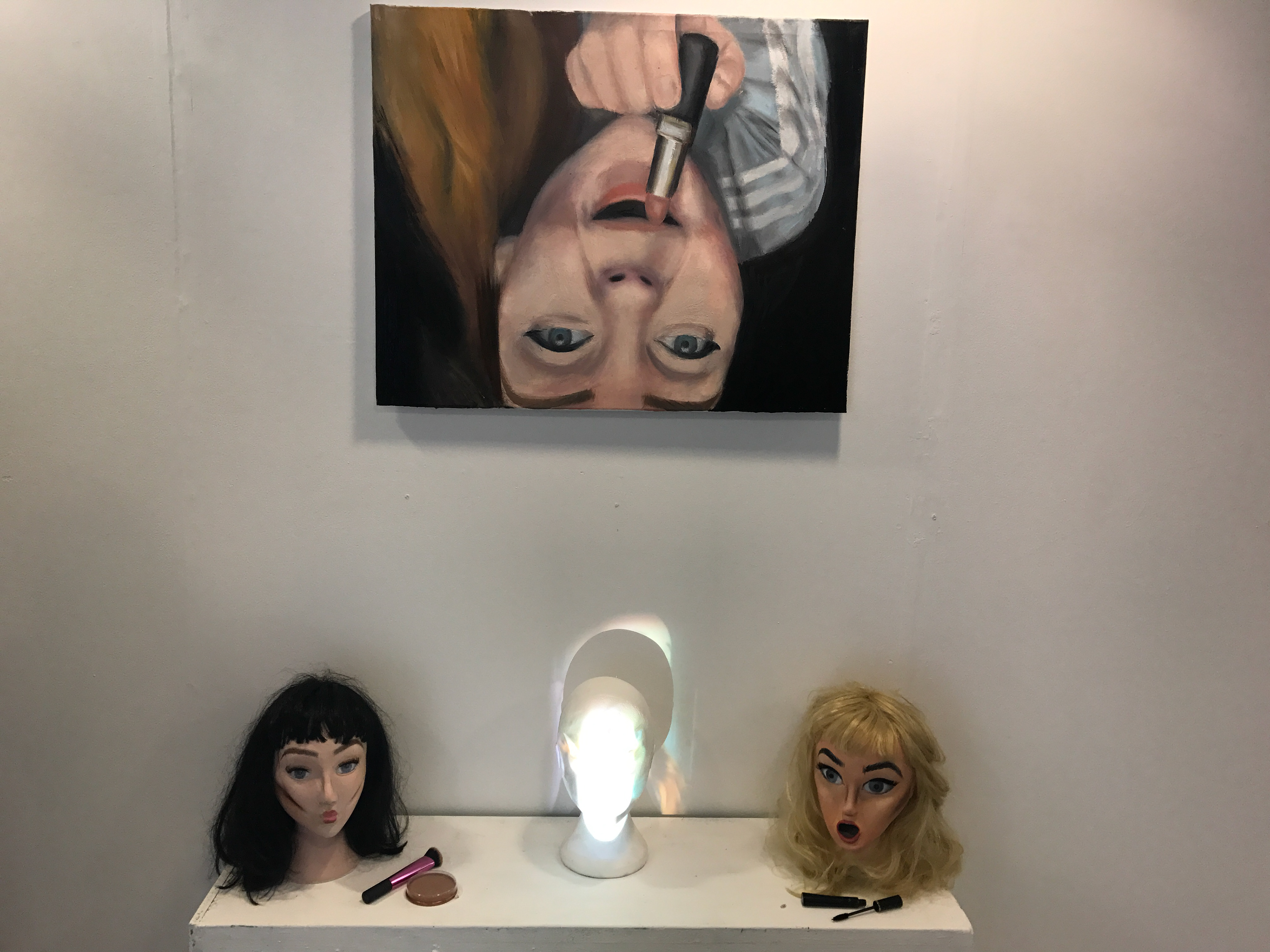 Face on, focuses on how ironic most women pull unusual faces in the process of looking beautiful, oil painting on wall, clay head on each side and time lapse projected on a polystyrene head in the middle