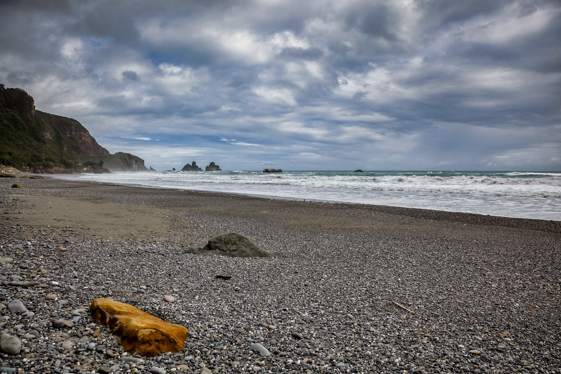Stormy weather approaching an orange rock on a beach in New Zealand