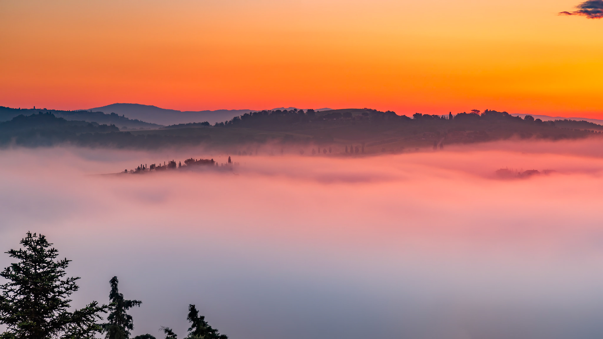 Early morning mist flooding the valleys of Tuscany at sunrise