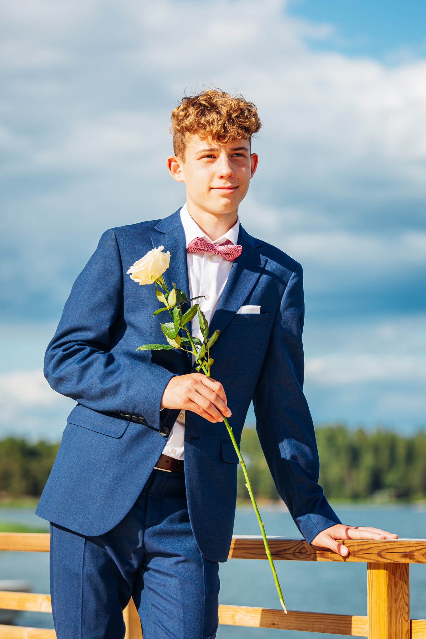 Kesäinen rippikuva meren rannalla, poika katsoo horisonttiin ruusu kädessä.