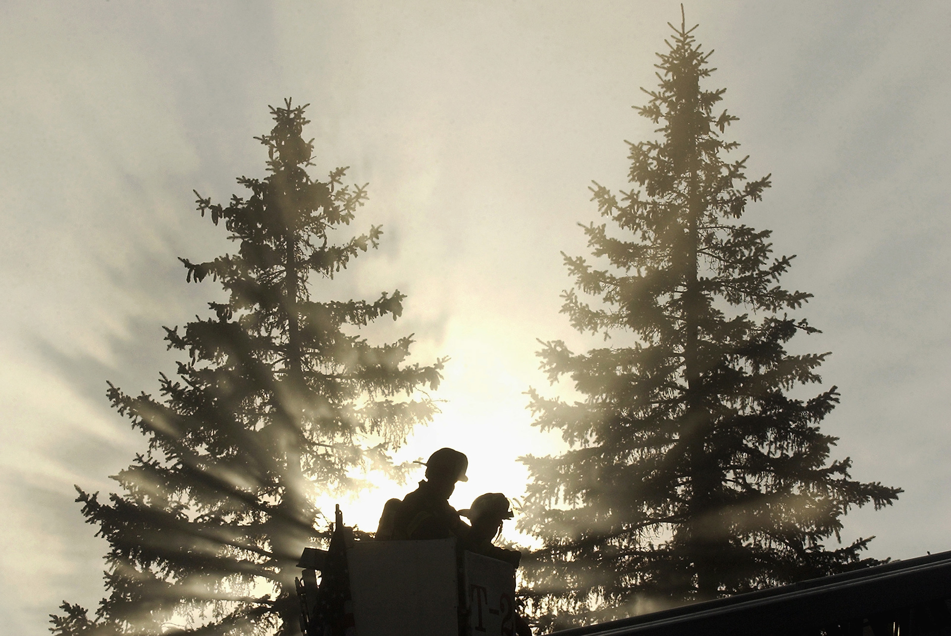 Brockton Fire Department Lt. Joe Solomon, left, and Mike Czaja are silhouetted as the sun pours through the branches of trees and creates shadows in the smoke from a house fire.