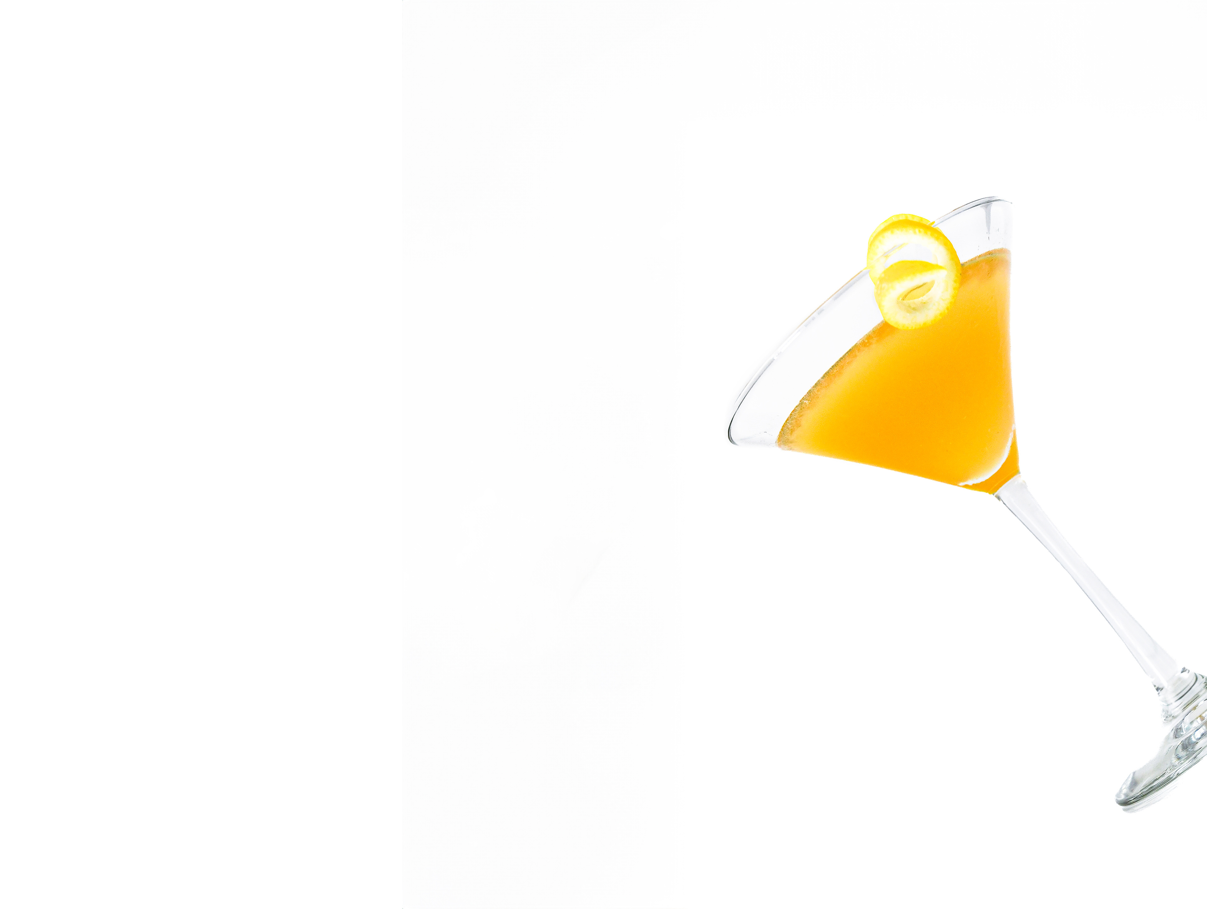 A Rum Sidecar cocktail elegantly presented in a martini glass, with a refreshing lemon peel garnish. The drink, made with rum, Cointreau, and freshly squeezed lemon juice, displays a clear, golden hue. The image captures the cocktail from a slightly angled view, showcasing the sleek glass and the vibrant lemon twist, set against a pristine white background.