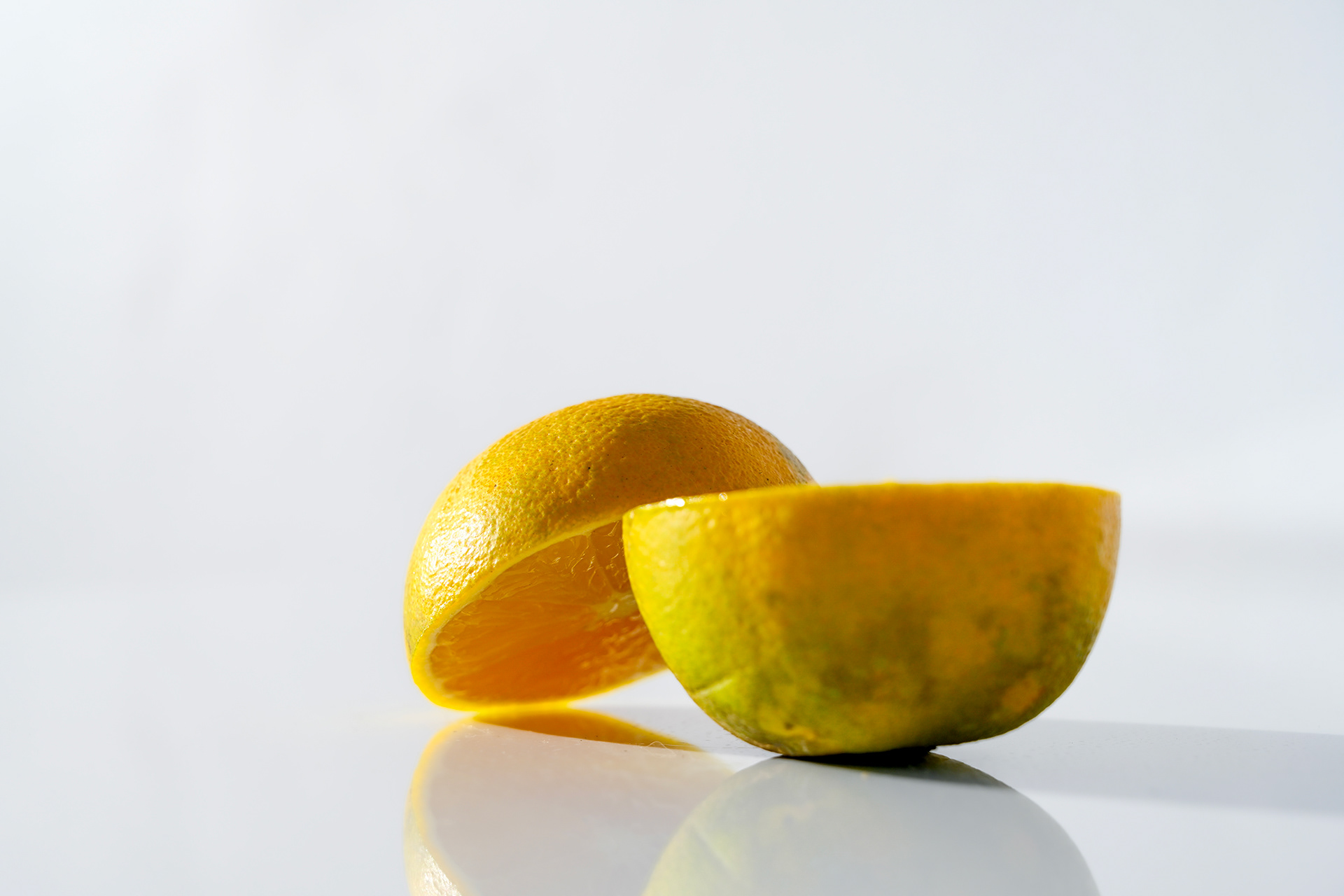 Half of a small green-yellow orange lying open to reveal its juicy center, with sunlight bringing out the natural color and texture.
