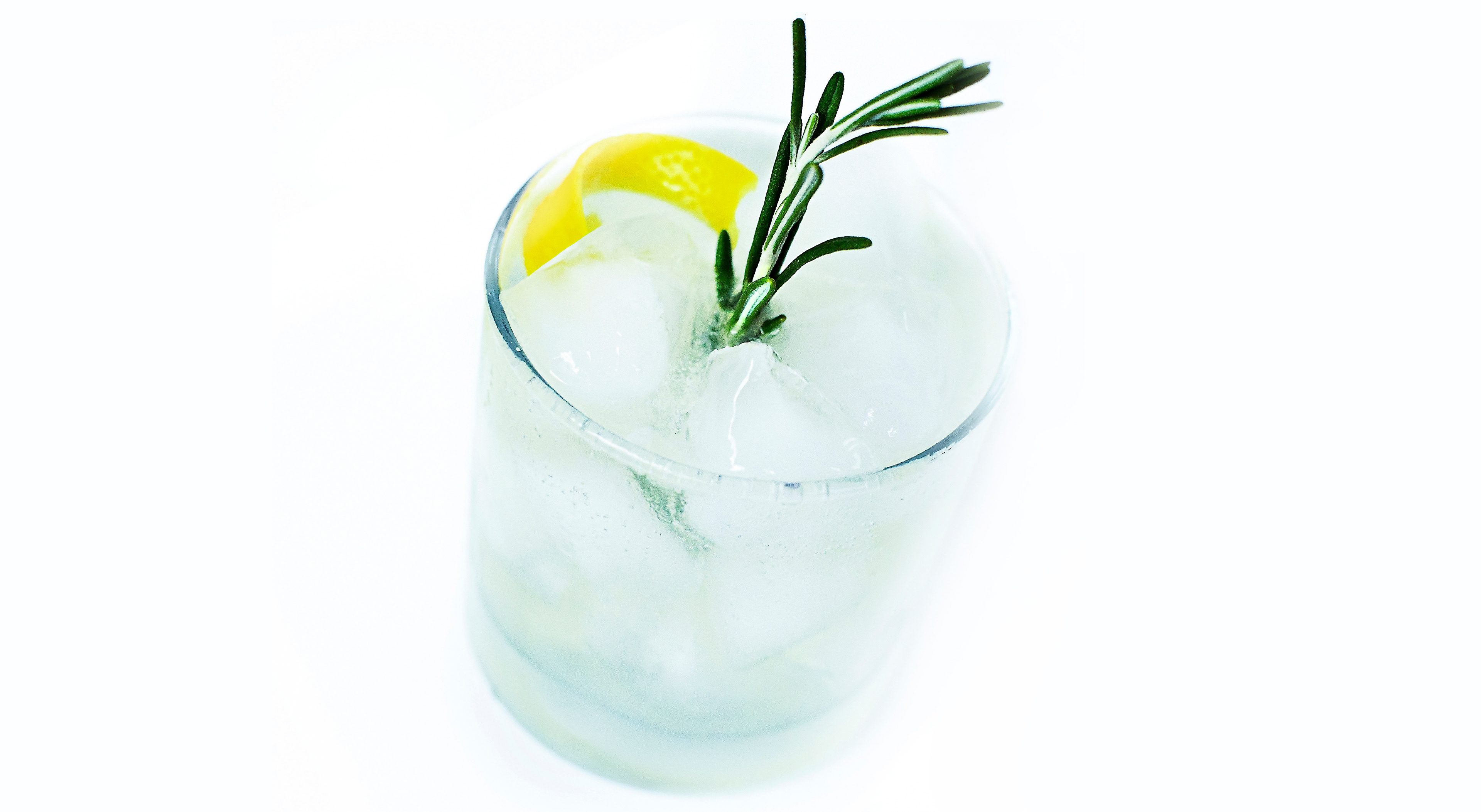A stylish Rosemary Tom Collins cocktail on a white background. The rock glass is filled with ice cubes and garnished with a lemon twist and a sprig of fresh rosemary. The drink, featuring lemon rosemary simple syrup, freshly squeezed lemon juice, and gin, is topped with club soda, showcasing a refreshing and aromatic twist on the classic Tom Collins. The vibrant colors and garnish highlight the unique and inviting flavors of this special version of the timeless cocktail.