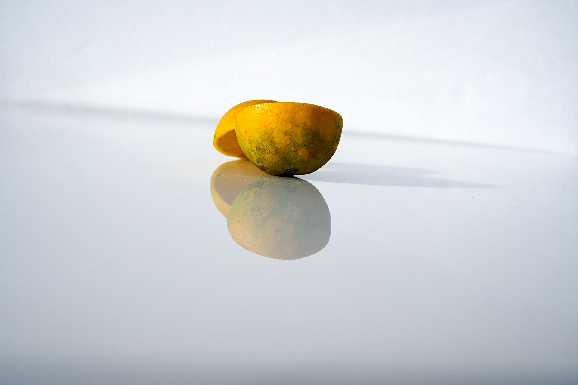 An orange arranged to show only its mottled green-and-yellow skin, with the juicy flesh subtly reflected in a mirror below, creating a layered and artistic composition.