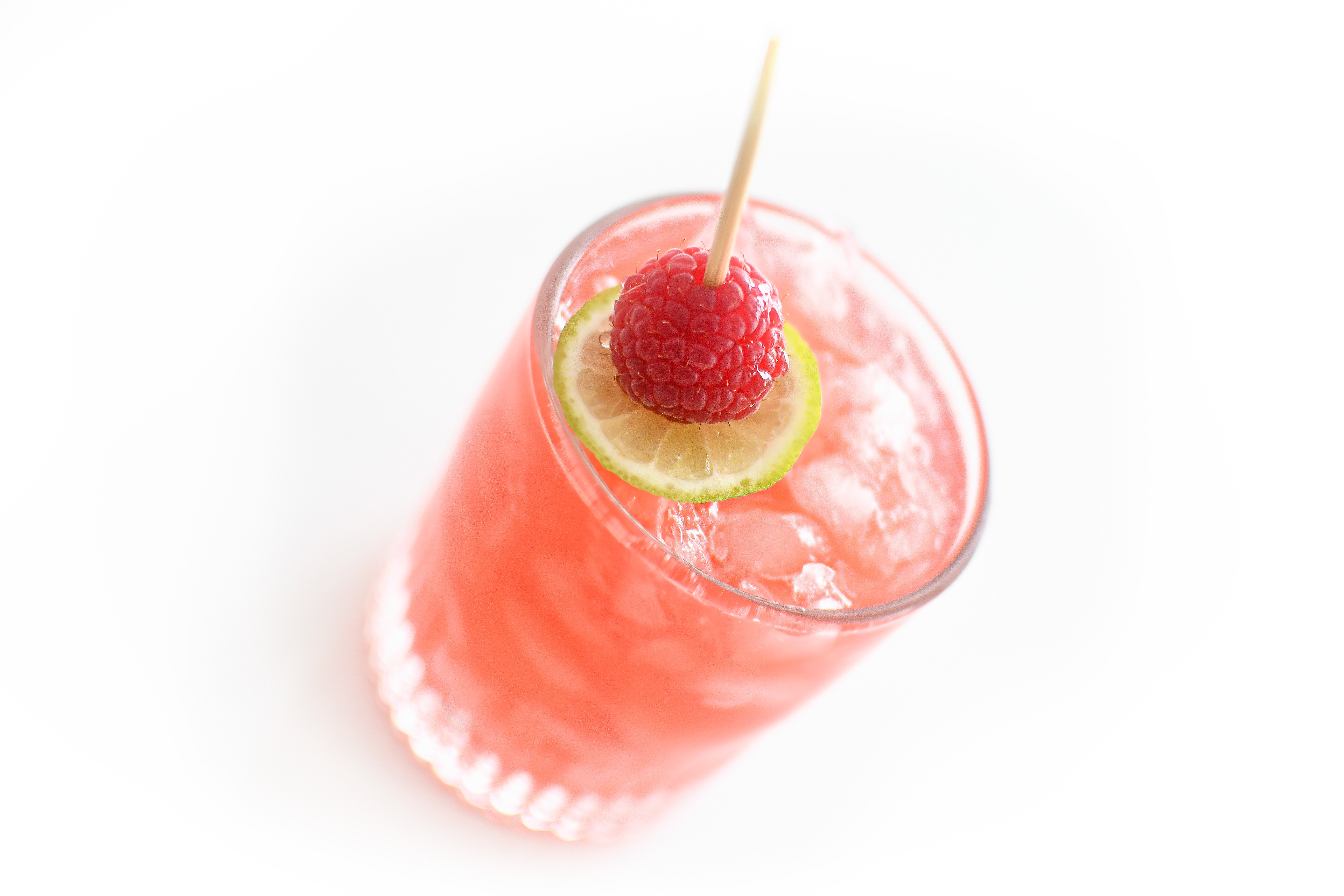 A close-up of a Knickerbocker cocktail on a white background, with a focus on the garnished rock glass filled with crushed ice. The cocktail, made with dark rum, Cointreau, Framboise, freshly squeezed lime juice, and fresh raspberries, is garnished with a lime wheel and a fresh raspberry. The image highlights the refreshing and vibrant nature of the drink, emphasizing the juicy raspberries and the perfectly chilled presentation.