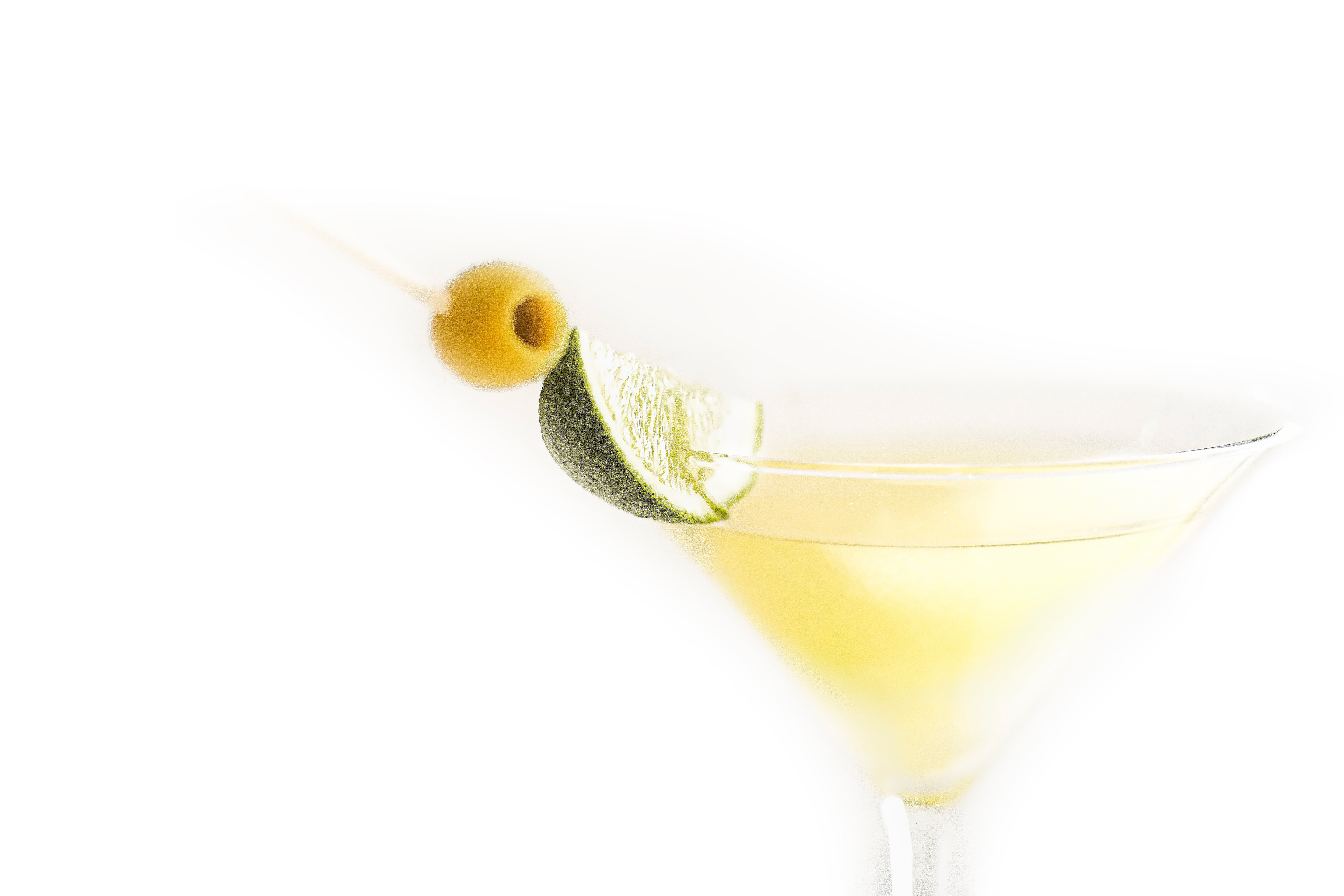 Close-up of a Mexican Martini served in a martini glass. The cocktail is garnished with a lime wedge and a green olive, against a white background.