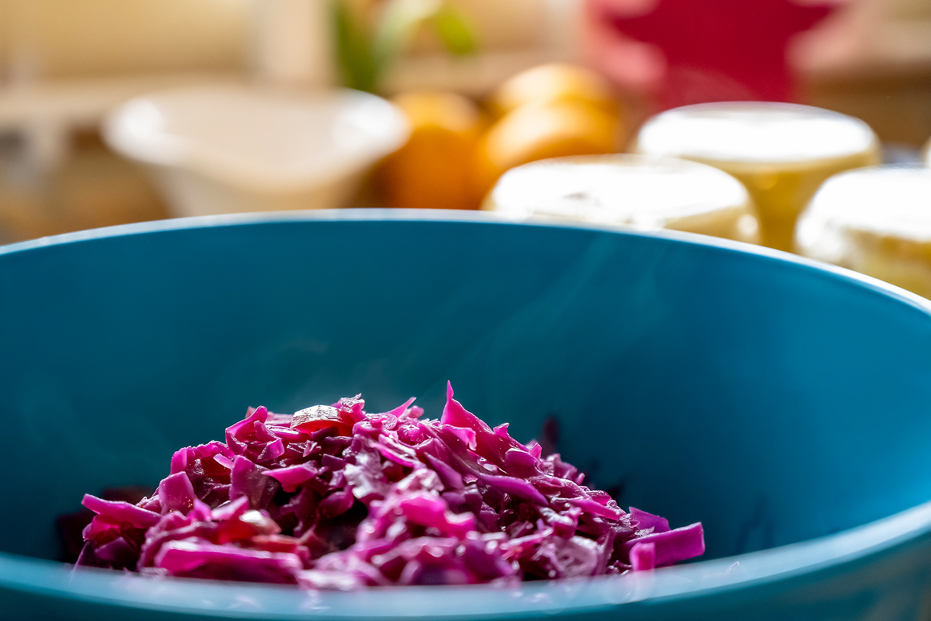 A vibrant bowl of freshly braised red cabbage sitting on a rustic wooden kitchen counter, cooling down to develop its tangy-sweet flavor. The dish is deep red with hints of apple pieces and onions, framed by soft natural light.
