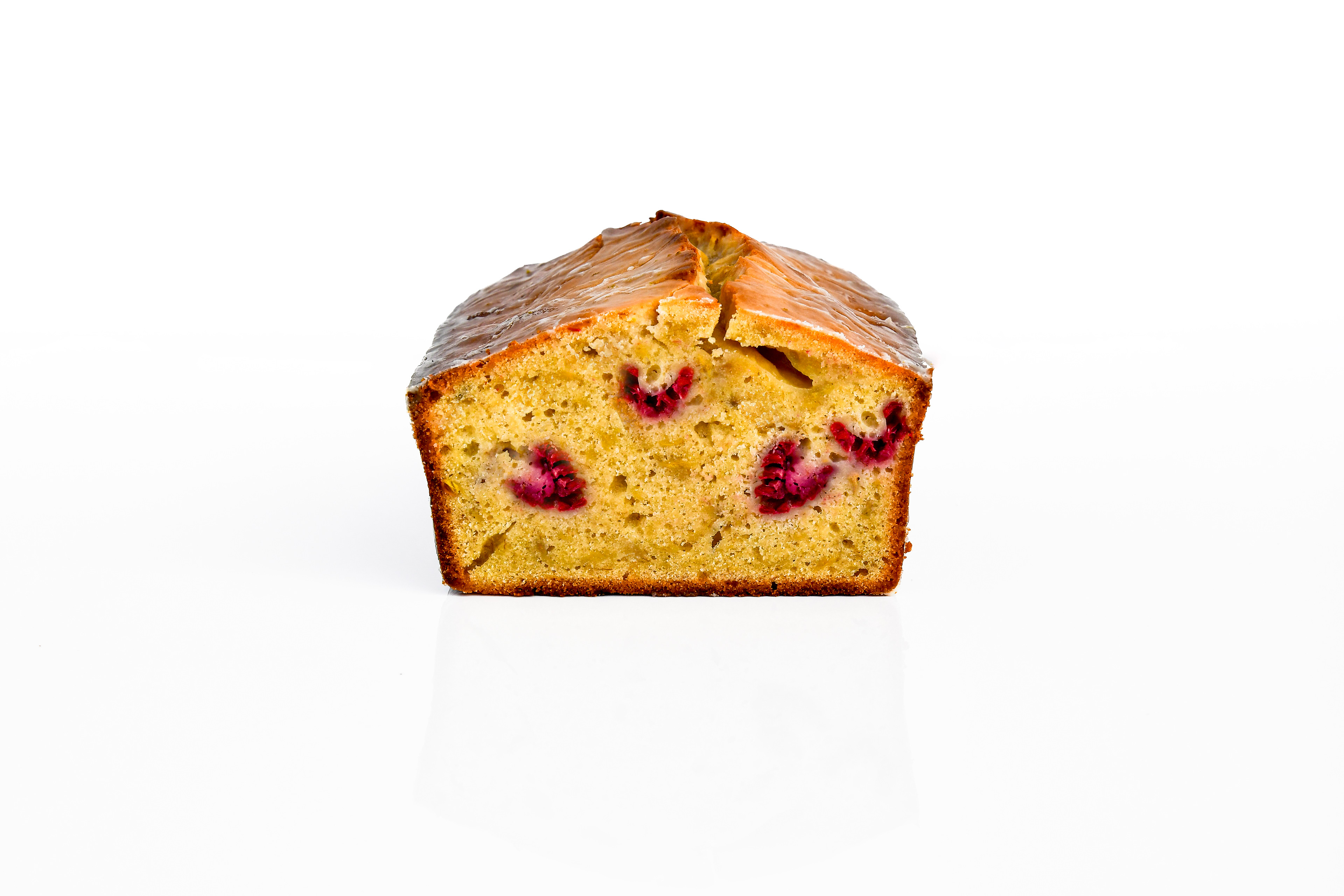 A golden banana raspberry lemon pound cake with a drizzle of lemon glaze, sliced to reveal a moist crumb with raspberry swirls, served on a wooden board with fresh raspberries on the side.