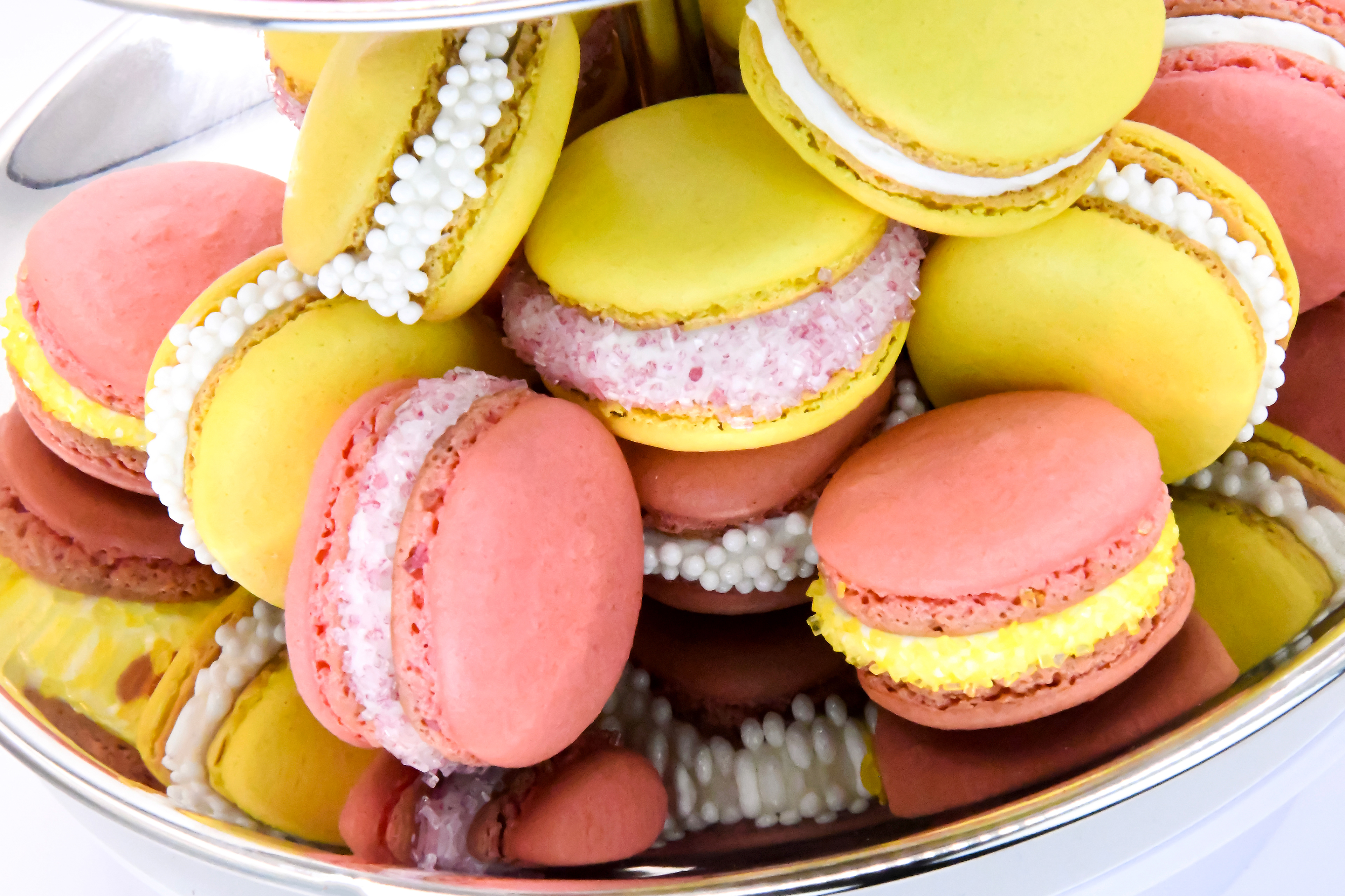 COLORFUL FRENCH MACARONS (YELLOW AND PINK) WITH A WHITE BUTTER CREAM FILLING ON NICELY DECORATED ON A ETAGERE WHITE BACKGROUND