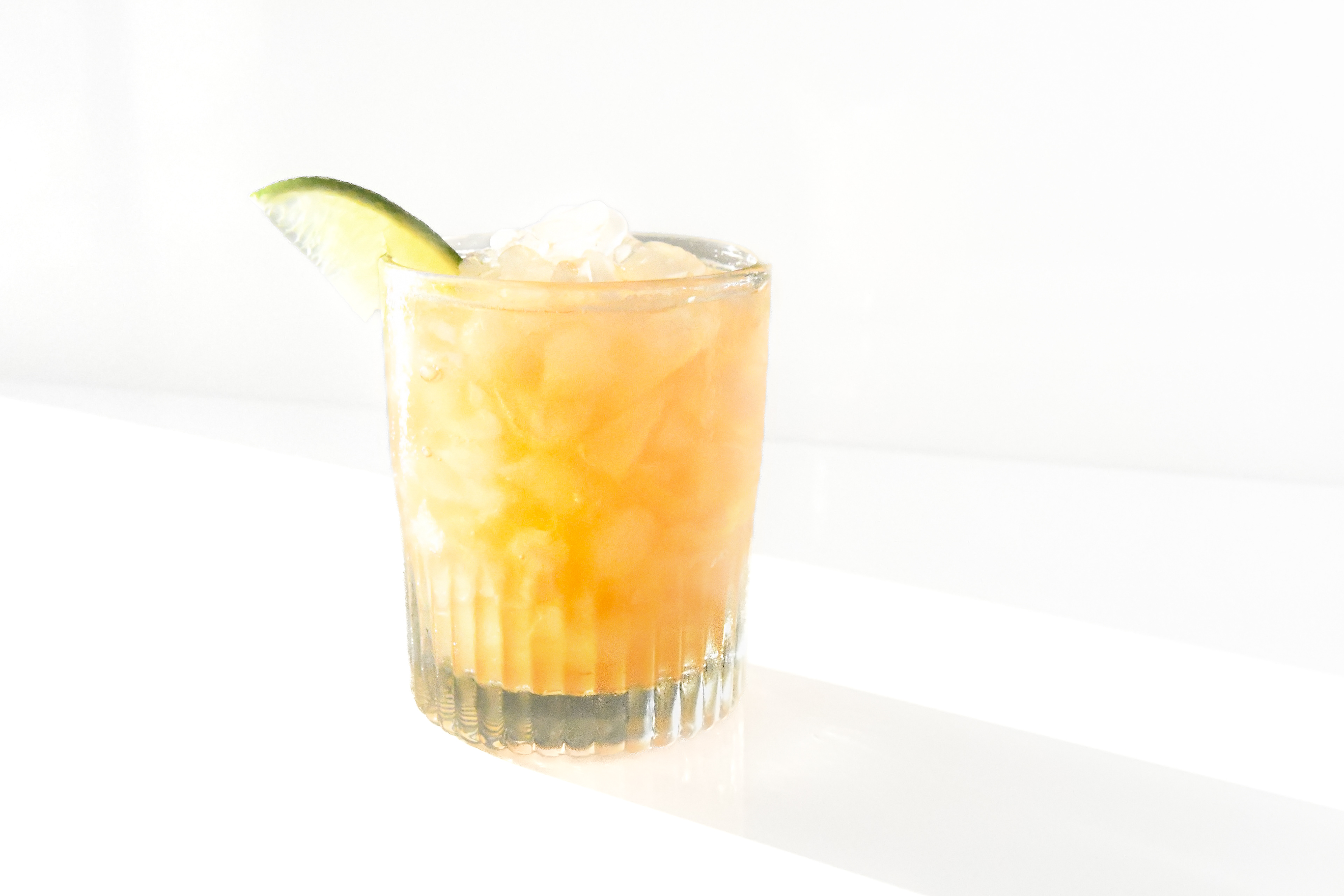 A Lavender Tequila cocktail presented in a rock glass, highlighting the vibrant color of the drink and the crystal-clear ice cubes. The cocktail, with its unique blend of chamomile-infused tequila reposado, lavender agave syrup, and freshly squeezed lime juice, is garnished with a slim lime slice. The image focuses on the elegant, chilled appearance of the drink, with a subtle, aromatic appeal, set against a pristine white background.