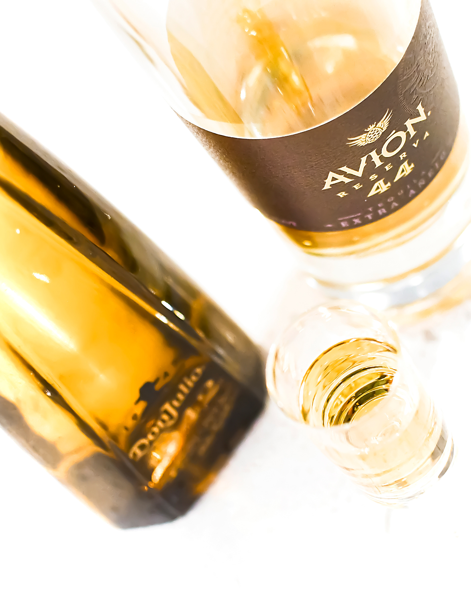 Two bottles of tequila displayed together: Don Julio and Avión 44. Both bottles feature golden and brown hues, with light shining through them. In front of the bottles, a glass of tequila is set, ready to be tasted.