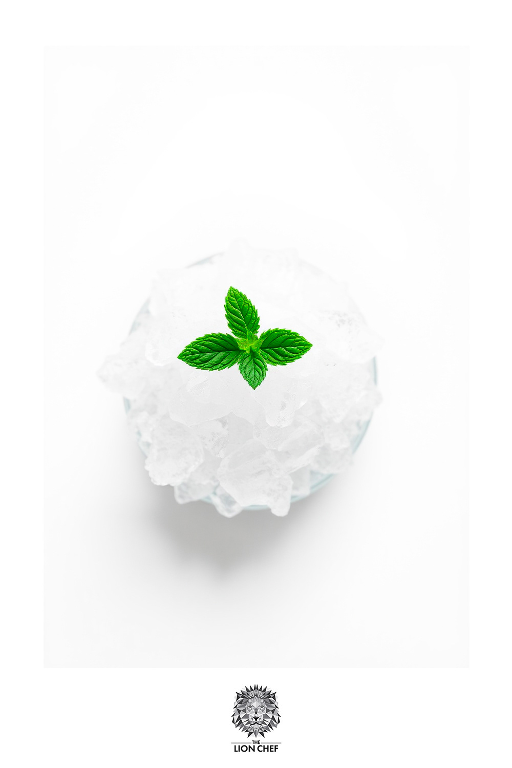 A clear glass filled with crushed ice, topped with fresh mint leaves, set against a clean white background. The shimmering ice contrasts beautifully with the vibrant green of the mint, creating a refreshing visual perfect for a summer cocktail.