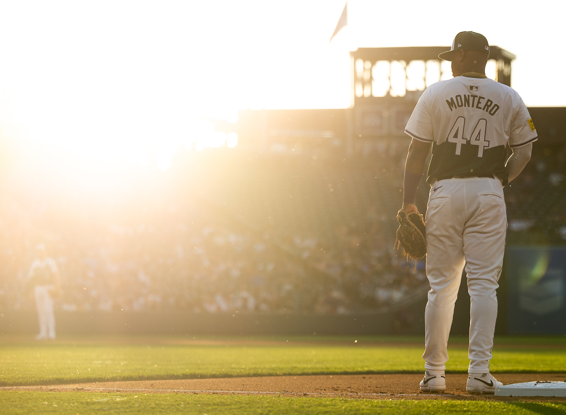 Colorado’s Elehuris Montero stands at first base bathed in golden light as the sun sets over Coors Field.