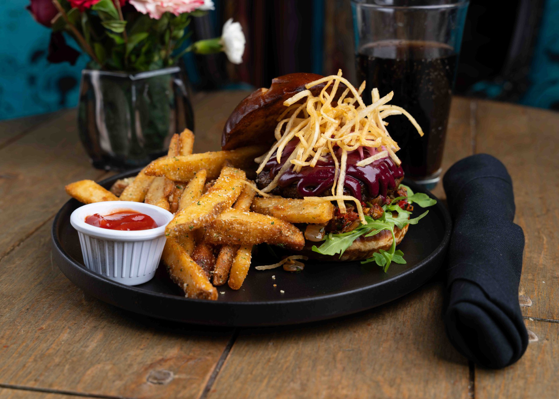 Black Tie Burger - Crawford's Bar & Grill - Brisket and petite tender grind sits atop arugula and warm bacon relish, finished with whipped Brie, pickled onion, Bumberry BBQ, and a crisp potato stack on a Dijonaisse-toasted pretzel bun.