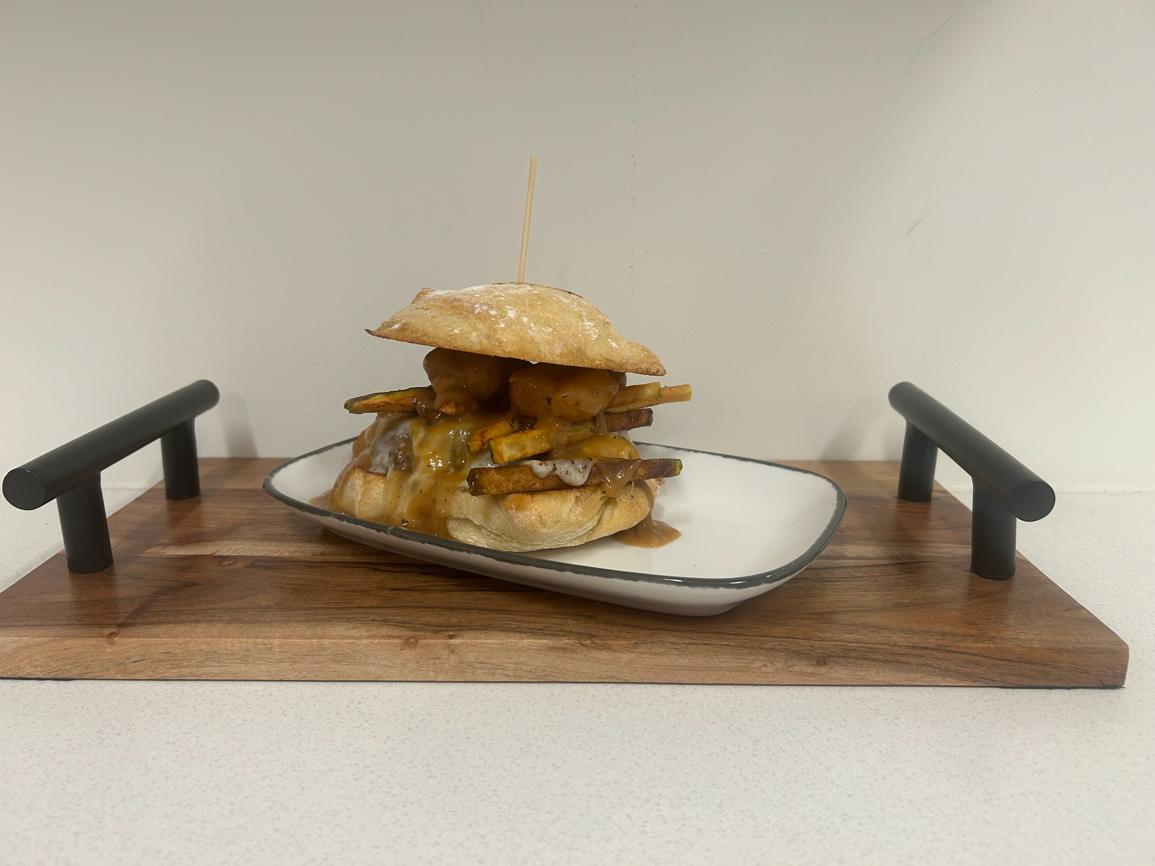 The Canadian Express - Cascata - 1/2lb Demkota Ranch Beef burger patty with fresh mozzarella, hand cut fries, cheese curds, brown gravy and chopped bacon all presented on a locally sourced Ciabatta bun, served with a side of truffle parm sidewinder fries.