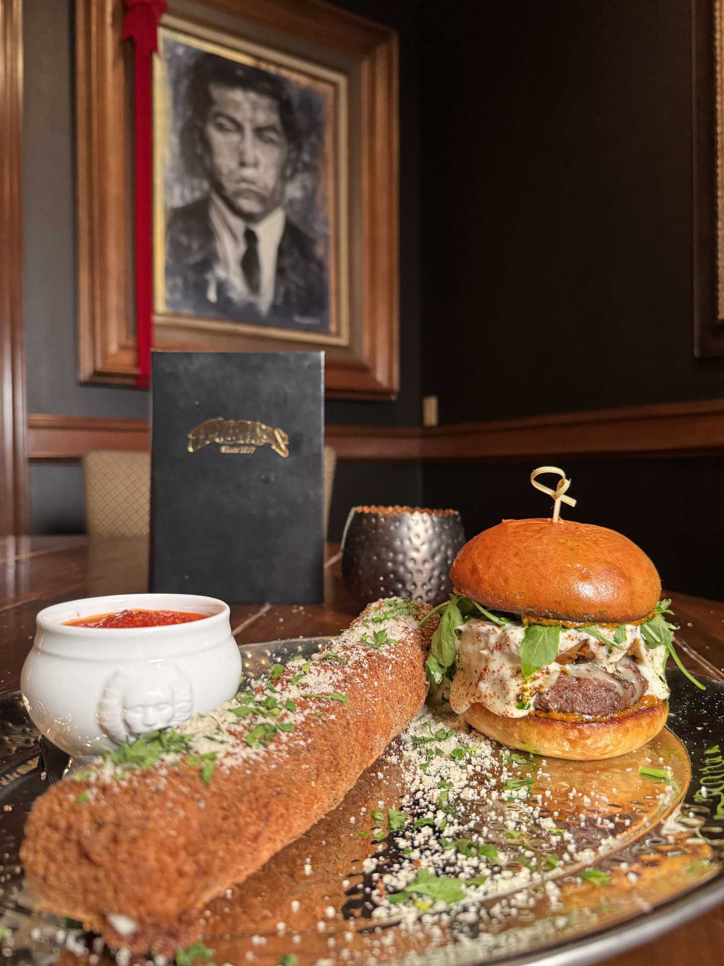 Don Corleone's Vendetta Royale: Minerva's Edition Burger - Minervas - Garlic Herb Brioche Bun, Sun-dried Tomato Basil Aioli, Prairie Coteau Lamb Ragu Bolognese, Hadrick Ranch Beef Patty, Mozzarella, Parmesan Fondue, Smoked Paprika, Cracked Black Pepper, Basil Oil, Served with Hand Breaded Jumbo Mobsterella Stick, Bold Marinara 