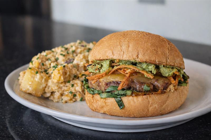 La Tormenta Burger - Perch - A 6 oz Tajin Seasoned Beef & Chorizo Patty topped with Pepperjack Cheese, House Guacamole, Pineapple Salsa, Ancho Aioli, Shrettuce, and Crispy Tortilla Strips. Served on a Custom Telero Roll produced by Breadico. Served with a side of Elote Potato Salad.