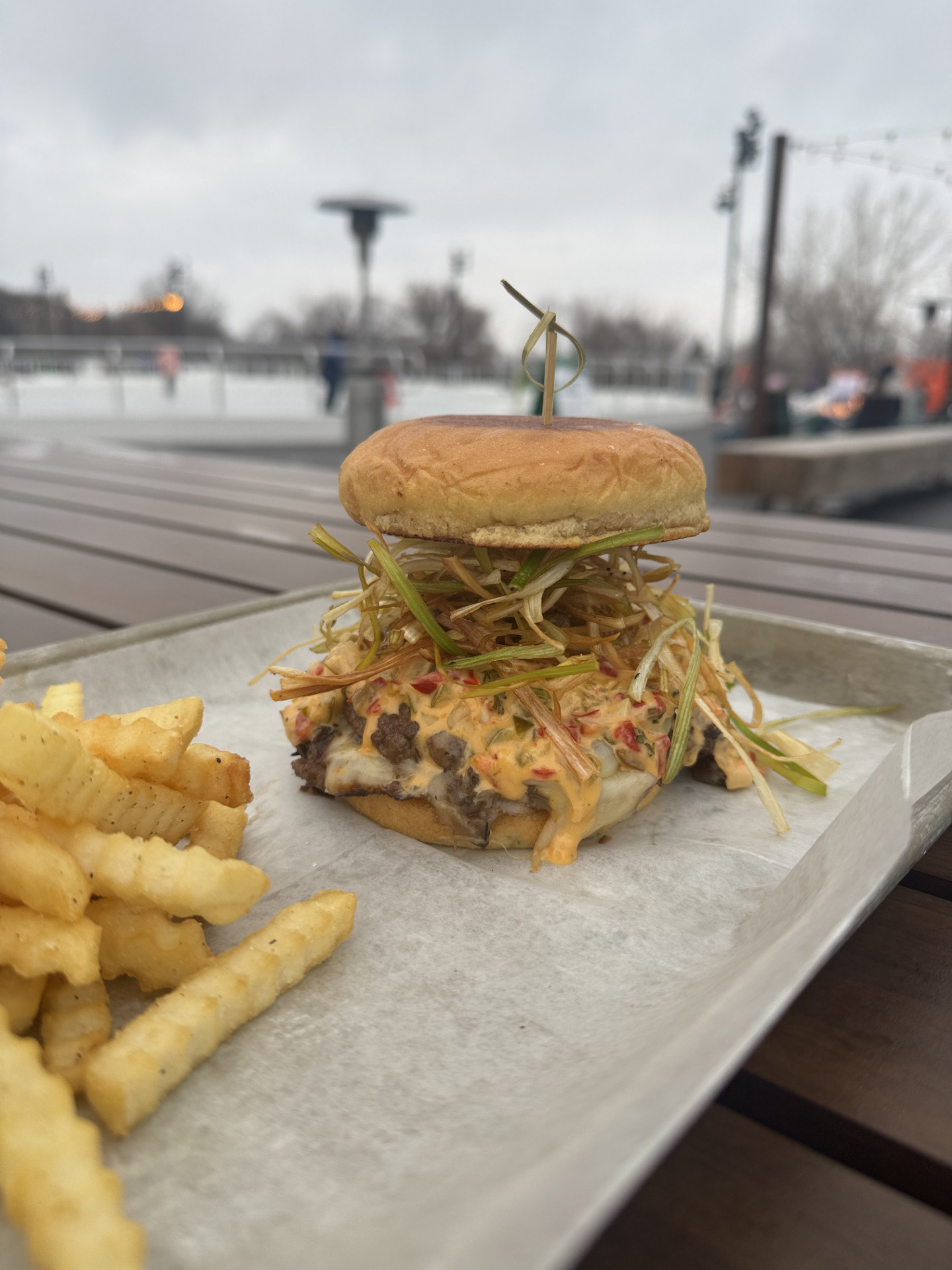 The Elk Burger - The Lodge Bar & Grill at Jacobson  Plaza - Elk smash patties, cherry pepper aioli, muenster cheese, and fried leeks on a potato bun. 