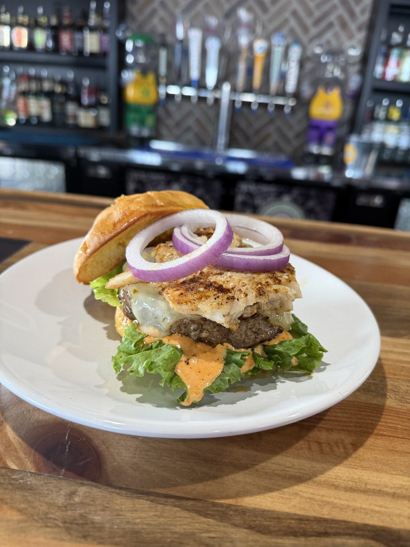 South Dakota Surf & Turf Burger - Shenanigans Sports Bar & Grill - 1/2lb Dakota pure bison beef patty topped withcajun dusted walleye, pepperjack cheese, and house-made spicy aioli. Finished with crisp leaf lettuce and red onion served on a grilled bun. 