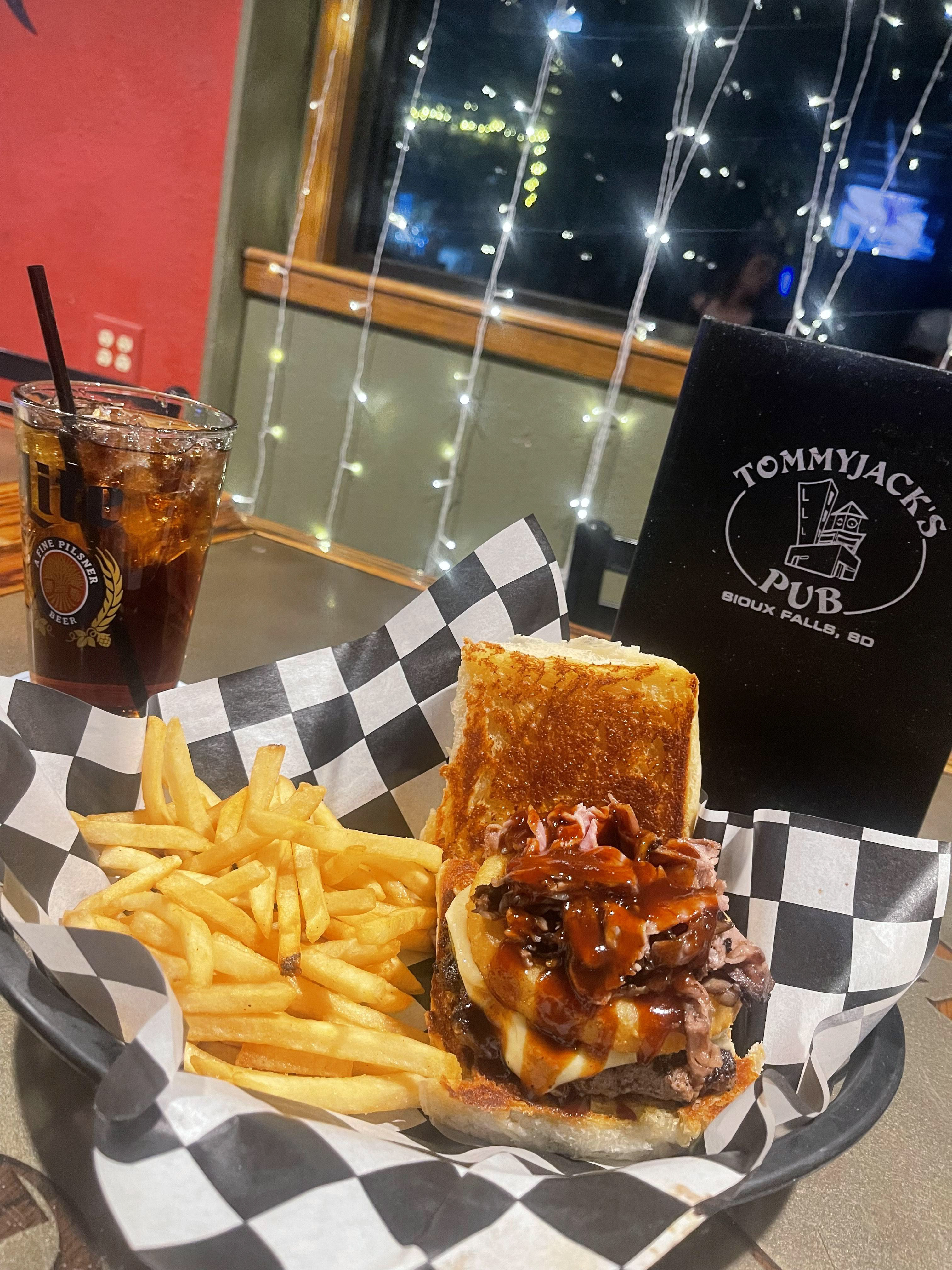 The Prime Time Burger - Tommy Jack's Pub - Fresh, hand-pattied 1/3 lb beef burger layered with melted pepper jack, and crowned with a crispy onion ring packed full of shaved prime rib, with a light kick of jalapeños, . Finished with a drizzle of housemade cherry barbecue sauce to hit the sweet-and-savory mark just right. Big flavor, bold bite, zero apologies — served with your choice of tots or fries. 