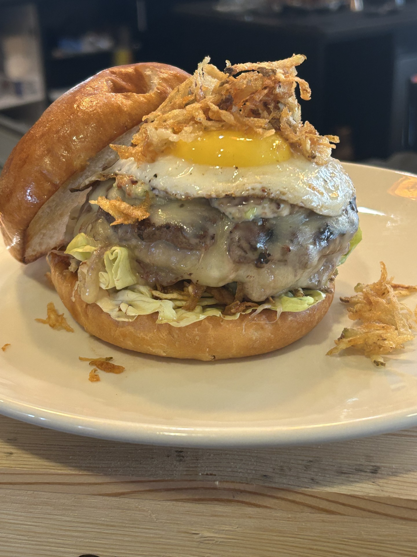 The Chosen Juan - CRAVE  - Juicy burger stuffed with Swiss cheese, topped with bacon aioli, over easy eggs and crispy fried hash browns, on a brioche bun. Served with a side of fries.