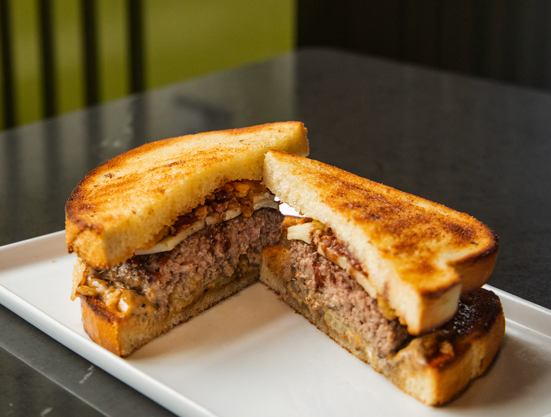 The Sonoma Sourdough - The Treasury - An 8 oz Certified Angus Beef patty on toasted sourdough with bubbling raclette, a rich bordelaise drizzle, black garlic aioli, and crispy shallots. Finished with fermented pickles for a bright, tangy pop that cuts through the richness. Wine-country flavors in burger form.