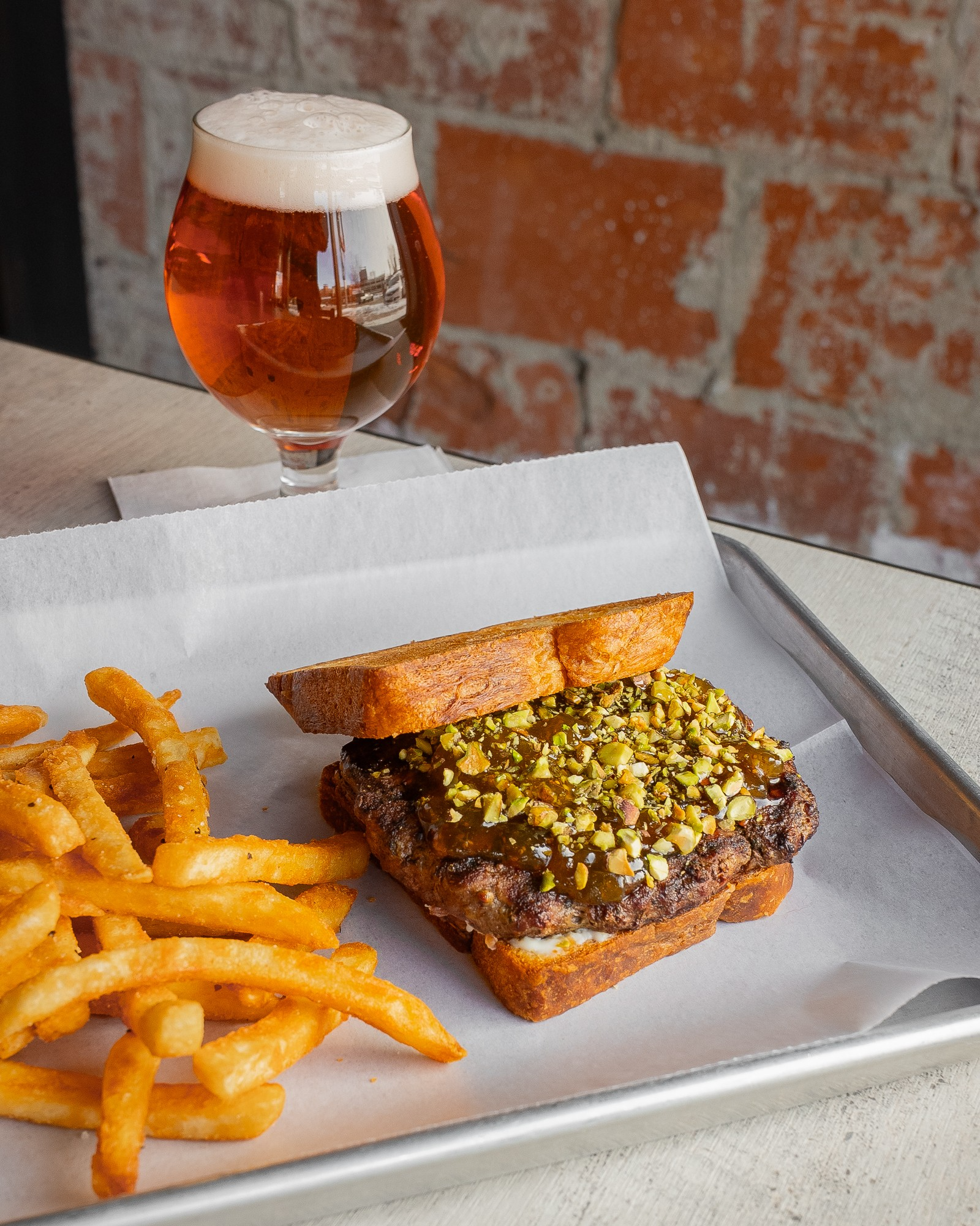 Fig Around & Find Out - PAve - 8 oz. Chuck steak burger topped with fig preserves, chopped pistachios, hot honey, and bacon cream cheese spread on a croissant bread bun. Served with choice of side. 