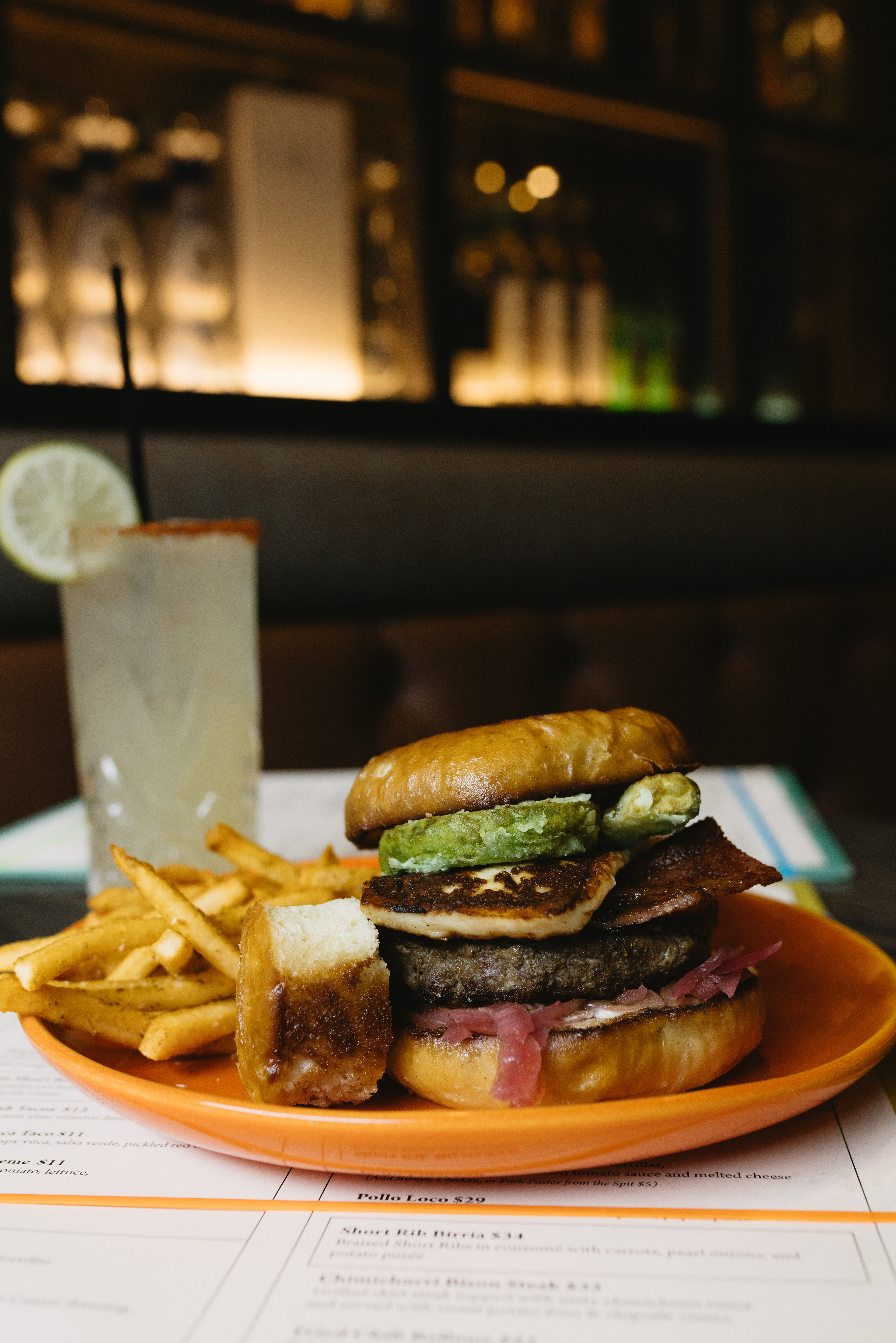 Avocado Sunrise - Dahlia Kitchen + Bar - Rise and Shine with our Avocado Sunrise, stacking an 8 oz beef patty with candied bacon, crispy deep fried avocado slices, queso fresco, pickled red onions and creamy poblano garlic aioli, all crowned with an over medium egg nestled into a soft brioche bun for a rich, crunchy and delightfully messy bite from start to finish.