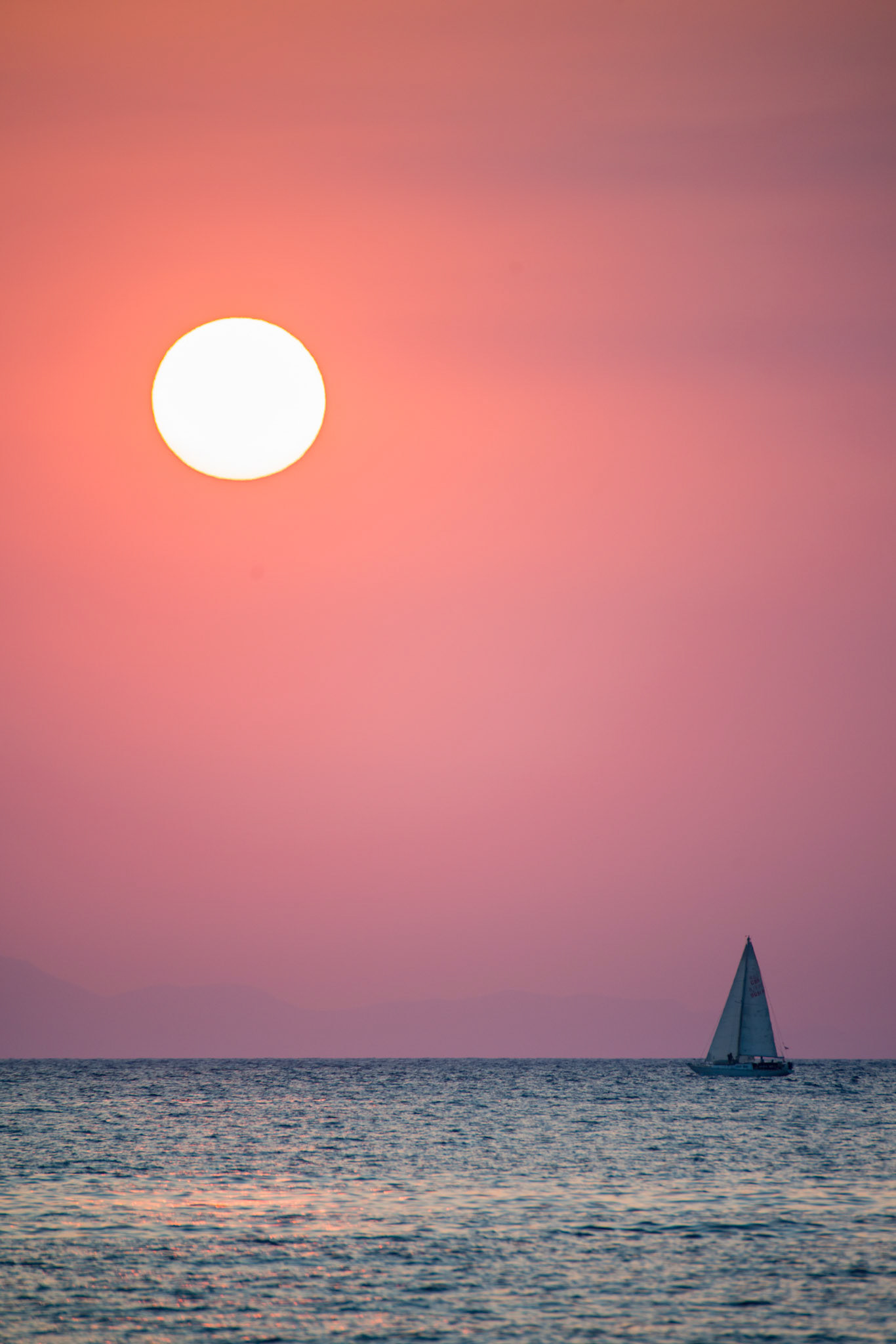 Seascape of a sailboat against the rising sun.