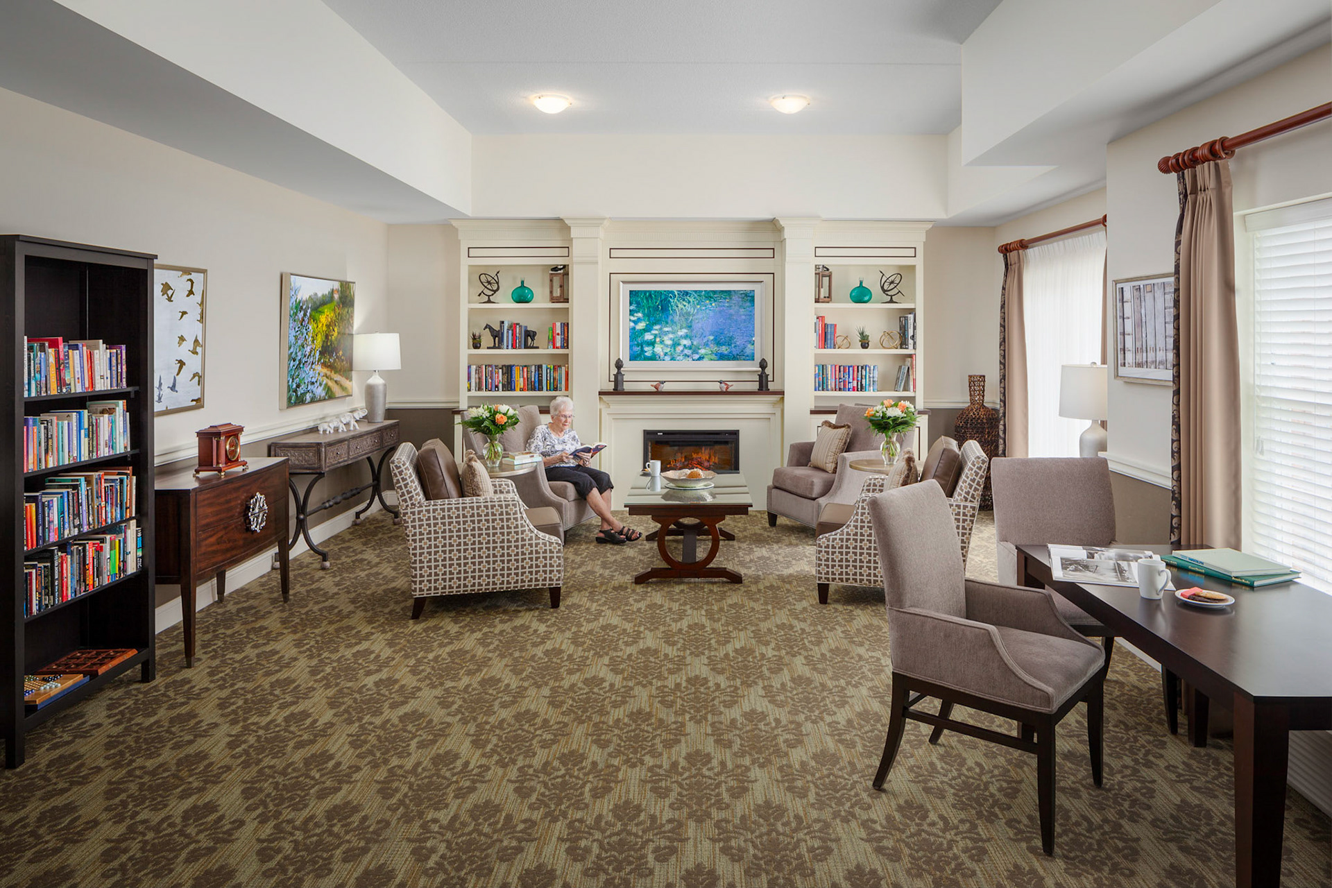A senior resident reading a book in a library next to the fireplace at Orchards Retirement Residence at Vineland, Ontario