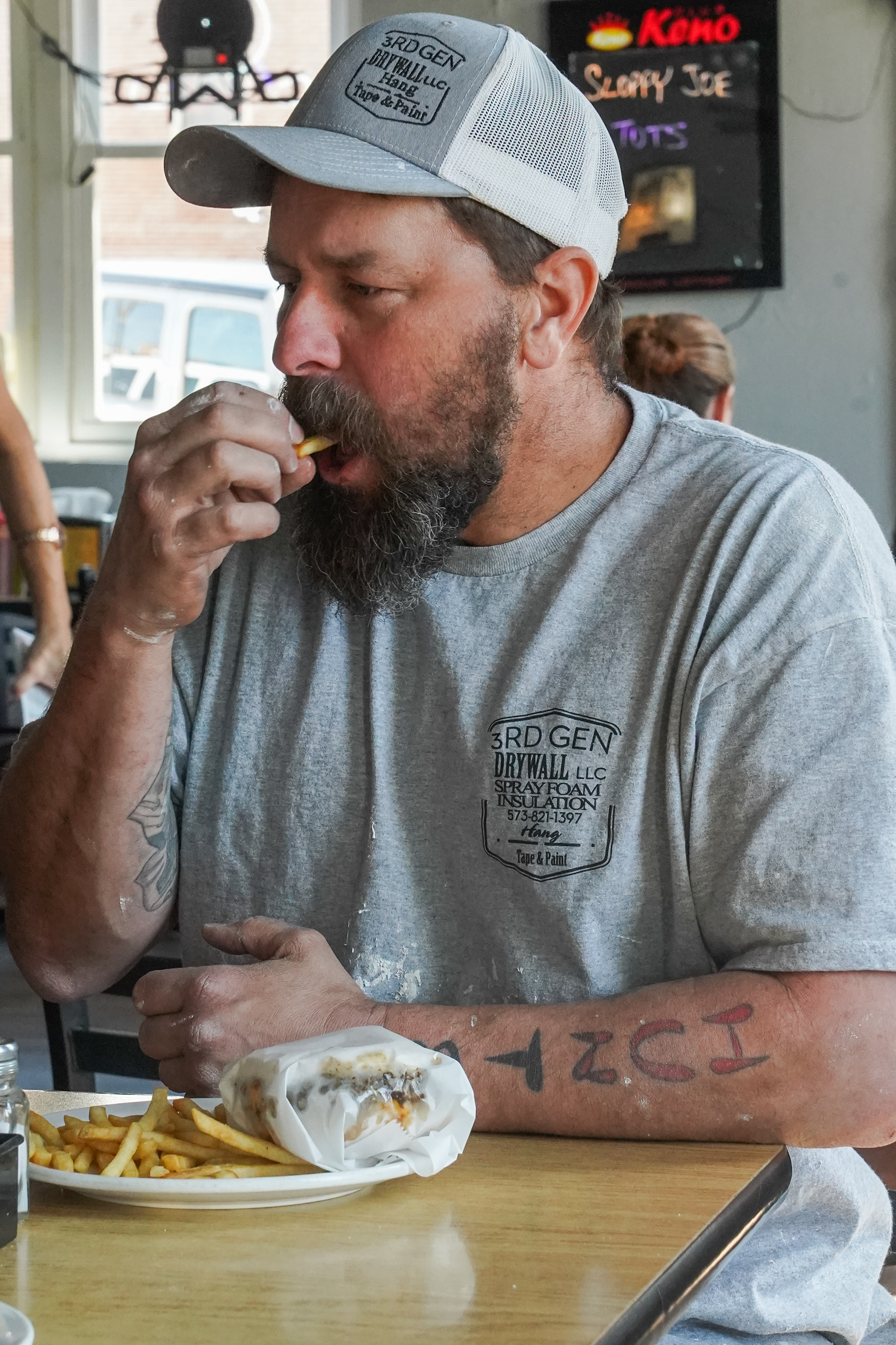 Brandon Shoemaker eats a Herbie burger and fries on Tuesday, March 19, 2024, at the Sharp Corner Tavern in Hermann, Mo. Shoemaker’s friend Andrew Portell joined him that afternoon. “There are forever people in Hermann” Portell said “Local people take care of local people.”