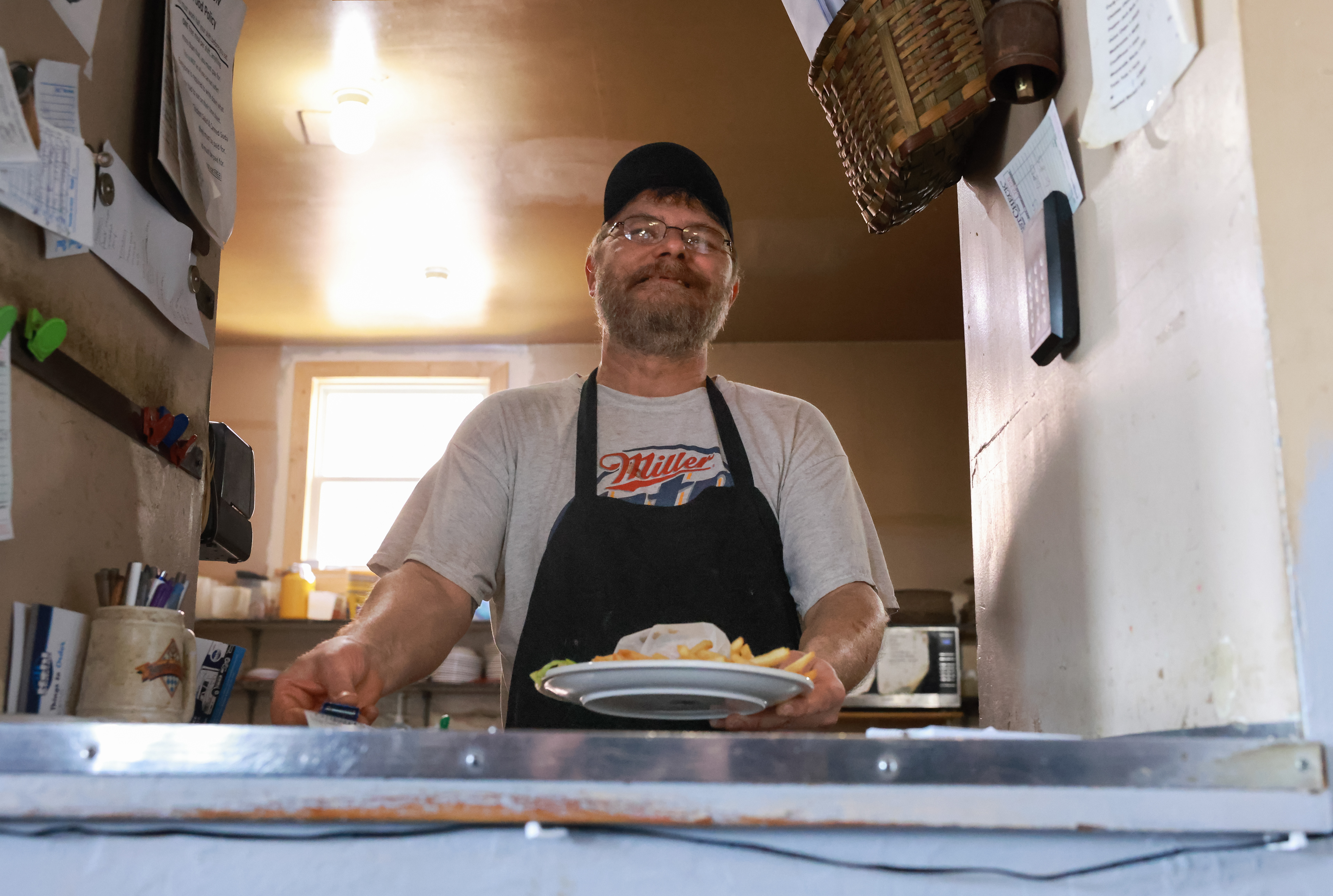 Toby Hoelmer places a burger and fries in the window on Tuesday, March 12, 2024, in Hermann, Mo. The Tavern is open all days of the week minus Sundays, closing only for inclement weather or the occasional construction project outside of the Tavern. If the Tavern does close, Toby will tell the people of Hermann on facebook, as well as texting regulars directly.