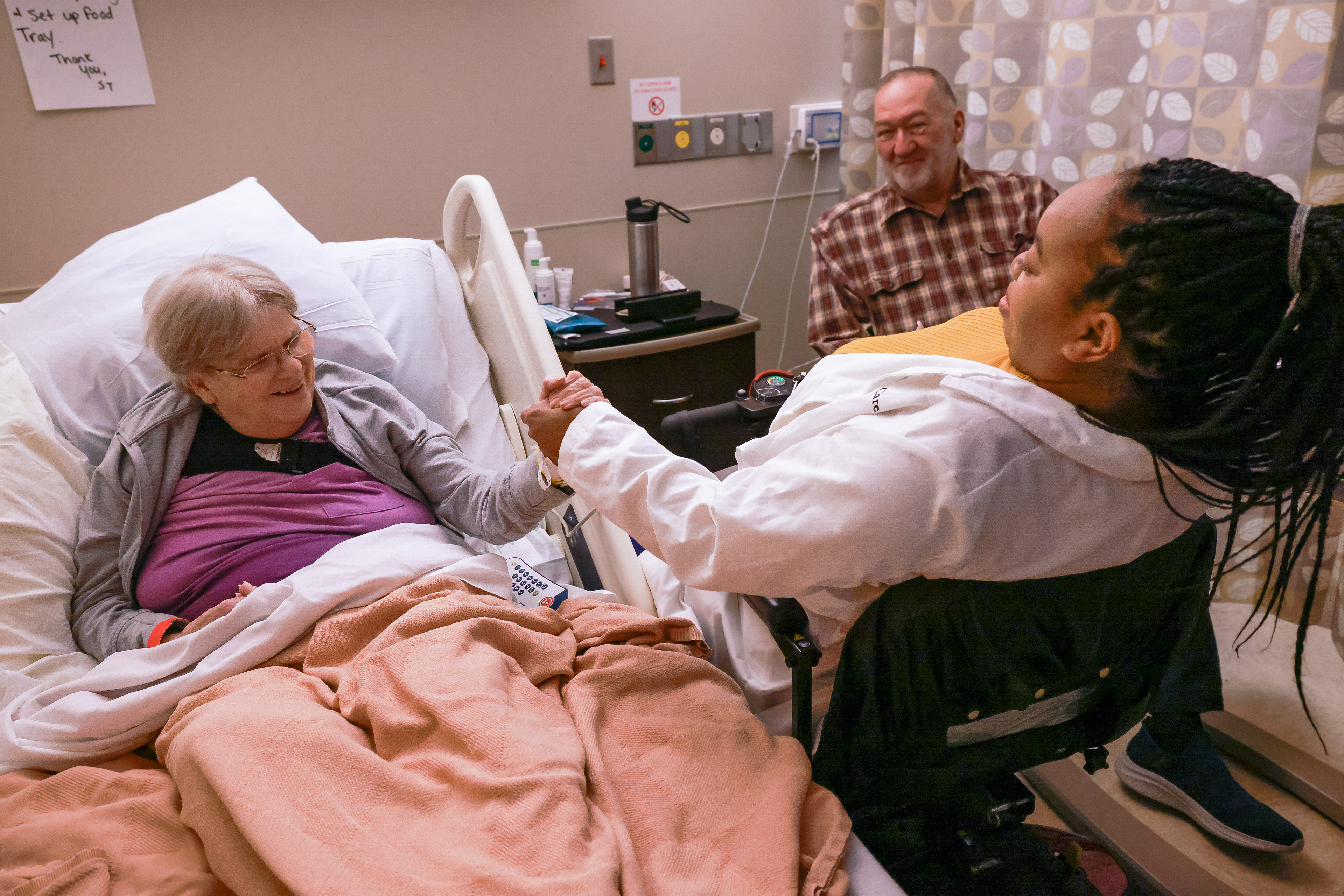 Glenda Stock, left, locks hands with Dr. Vovanti Jones, right, to test her strength while her husband, David Stock, center, watches on Feb. 16 at Rusk Rehabilitation Hospital in Columbia, Mo. Jones is a doctor who specializes in physical medicine and rehabilitation. She leads her patients and co-workers by example, having been diagnosed with Limb-Girdle Muscular Dystrophy at age 20. 