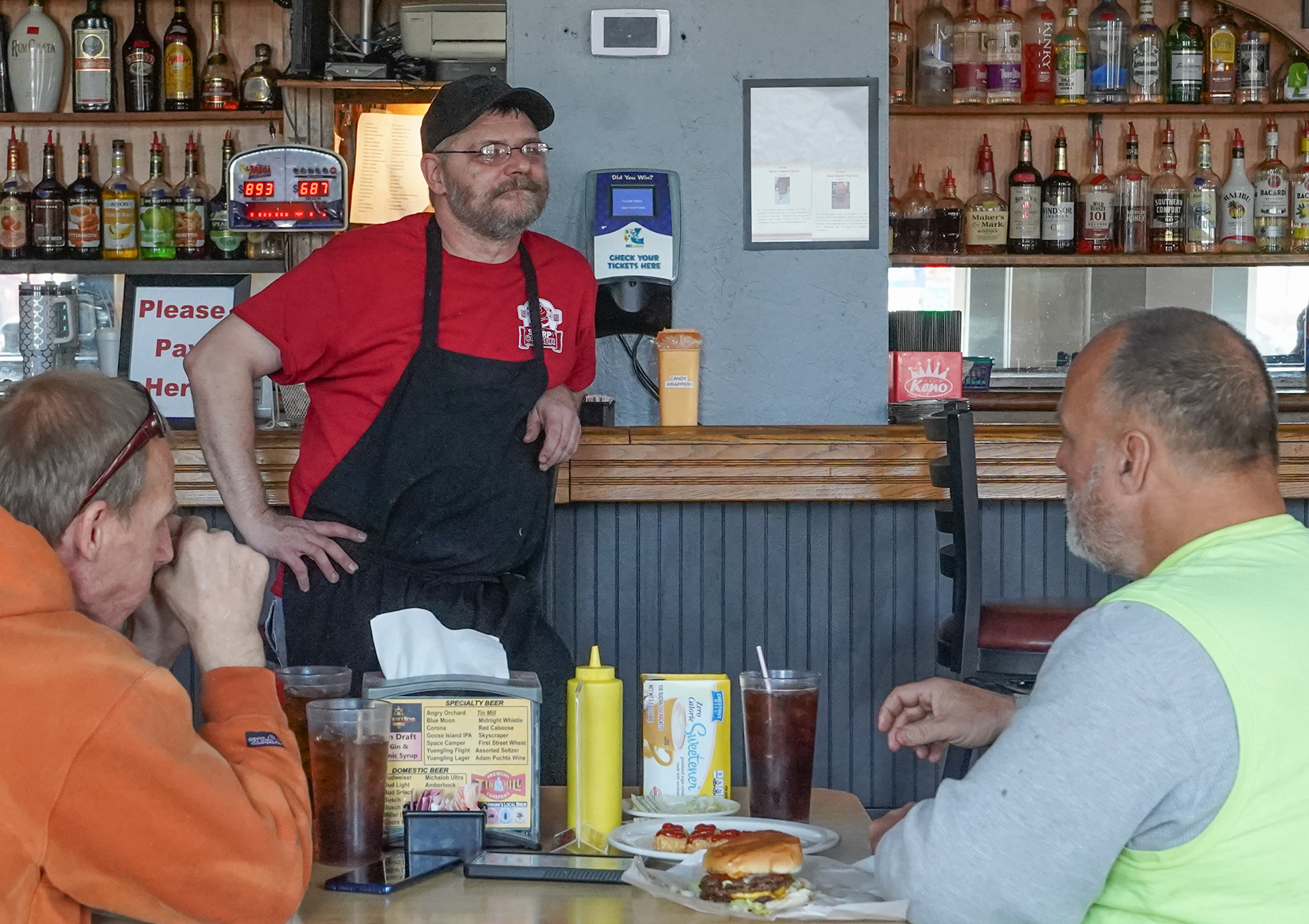 Toby Hoelmer takes a break from the kitchen to talk to Todd Ree, left, and Bradford Kohlbusch, right on Tuesday, March 19, 2024, in Hermann, Mo. Ree and Kohlbusch are two of many regulars at the Tavern, many of which the Tavern staff has names and orders committed to memory.