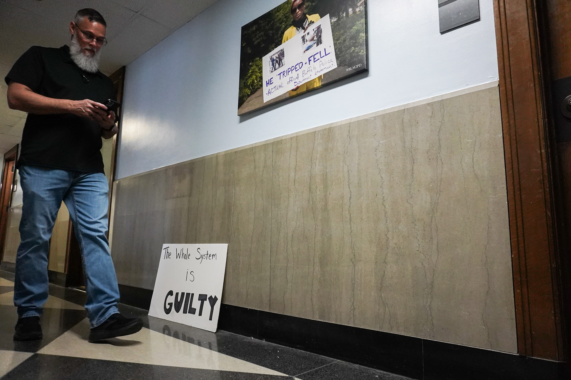 Scott Nistler, St. Louis trial office public defender investigator, walks down the hallway of one the office complex on Tuesday, March 25, 2025, in St. Louis. The sign on the floor and the photo on the wall are remnants of a Public Defender Demonstration and March during the summer of 2020 in protest police brutality. Public defender systems often see themselves as more than just employees, but advocates for social justice. Defending clients who cannot afford to defend themselves is often seen as a check on the unjust institution that is the criminal justice system.