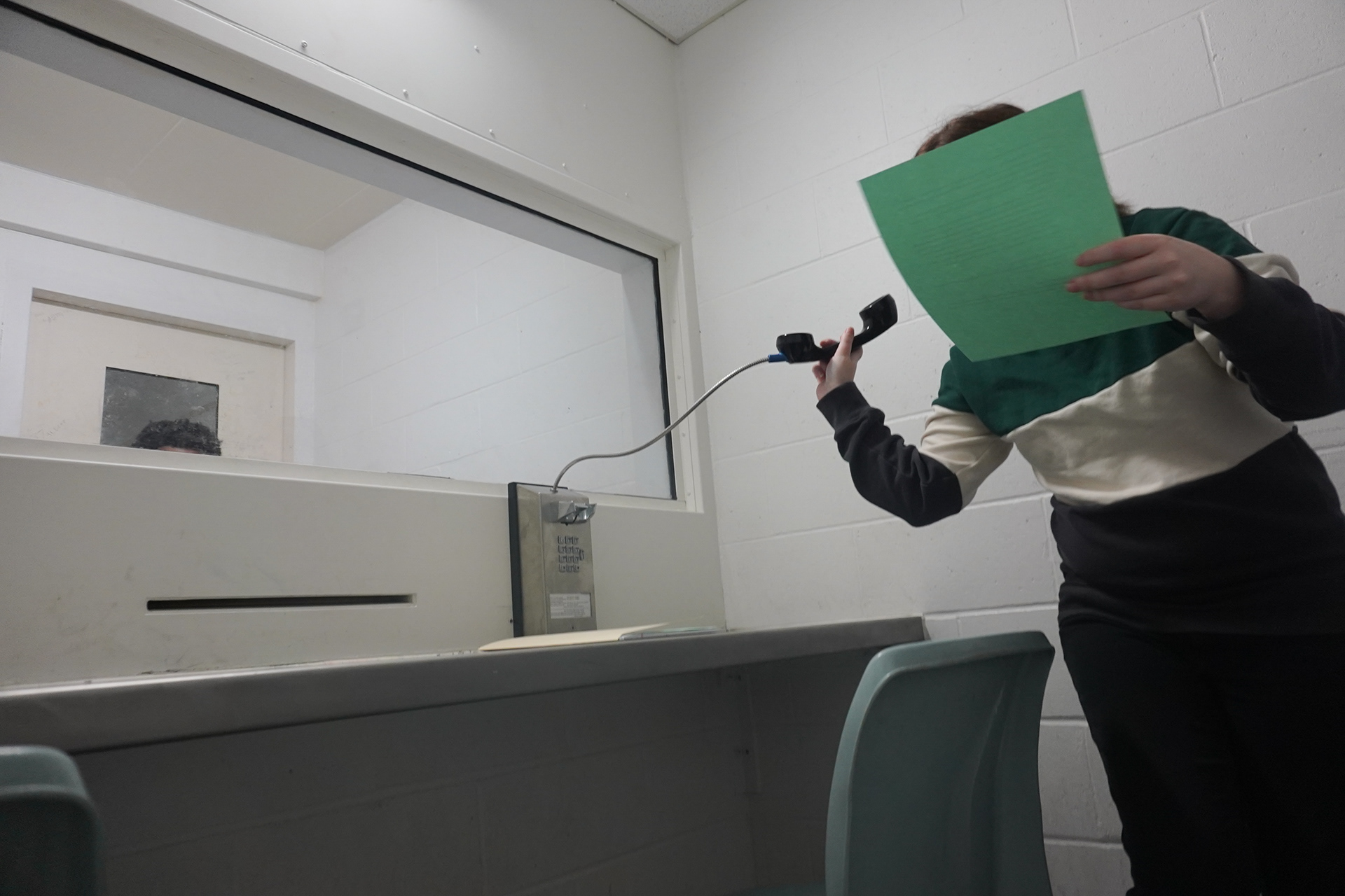 Emily Lucas, Lewis’ fellow full-time social worker in the St. Louis area offices, moves to show a client in the city jail a paper with homeless shelter resources on Wednesday, Feb. 26, 2025, in St. Louis. When not in the office talking with attorneys or in meetings, social workers go to jail often to visit clients. Visitation of clients within the jail is either a contact room, where they are in the same space, or the non-contact room, where they are separated by a small slit and a phone. The overwhelming case load and the bureaucracy of the city jail often make it hard for the social workers to see all the clients they need to help in time.   
