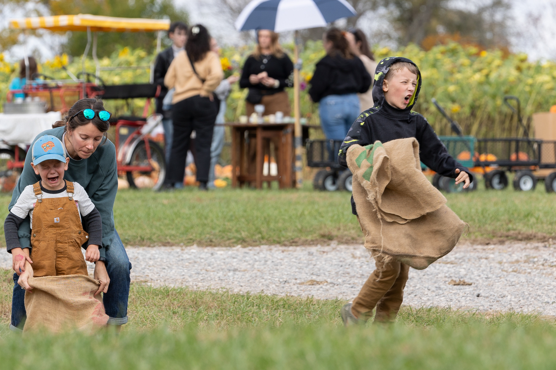 A mother tries to console her crying son as his brother walks off after winning their potato sack race at Libby's Pumpkin Patch Oct. 21, 2023.