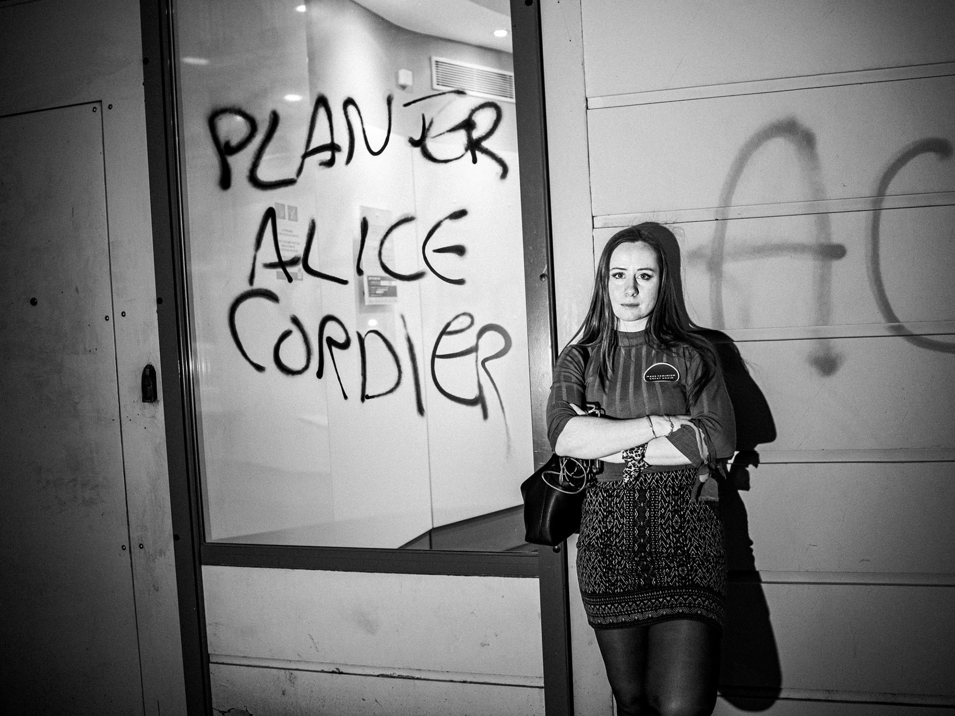 Paris, Alice Cordier, fondatrice du Collectif Nemesis pose devant un mur ou il y a inscrit Planter Alice Cordier, 2025.