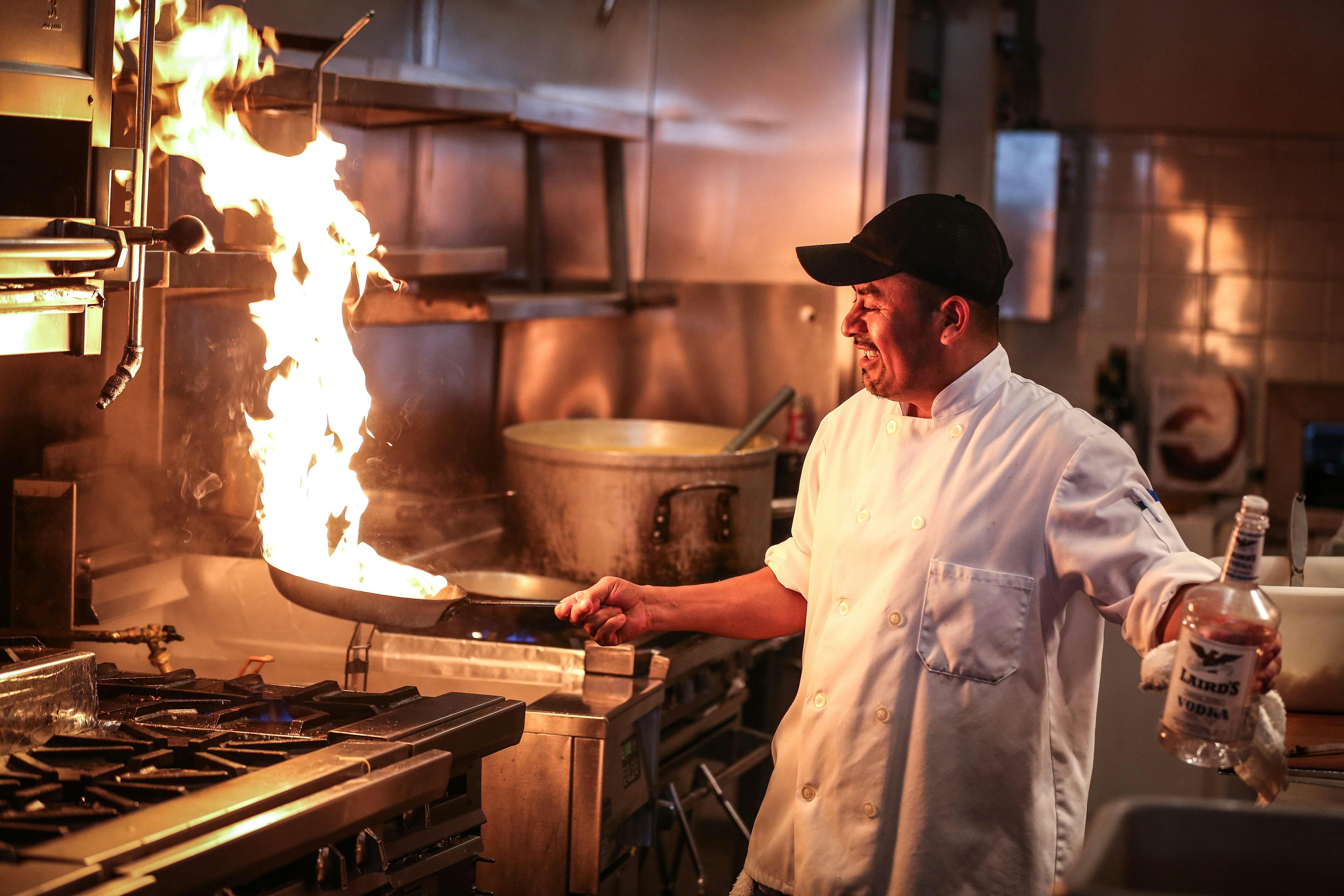 A laughing chef holds a burning pan in his hand / The Gastro Label / www.gastro-label.com