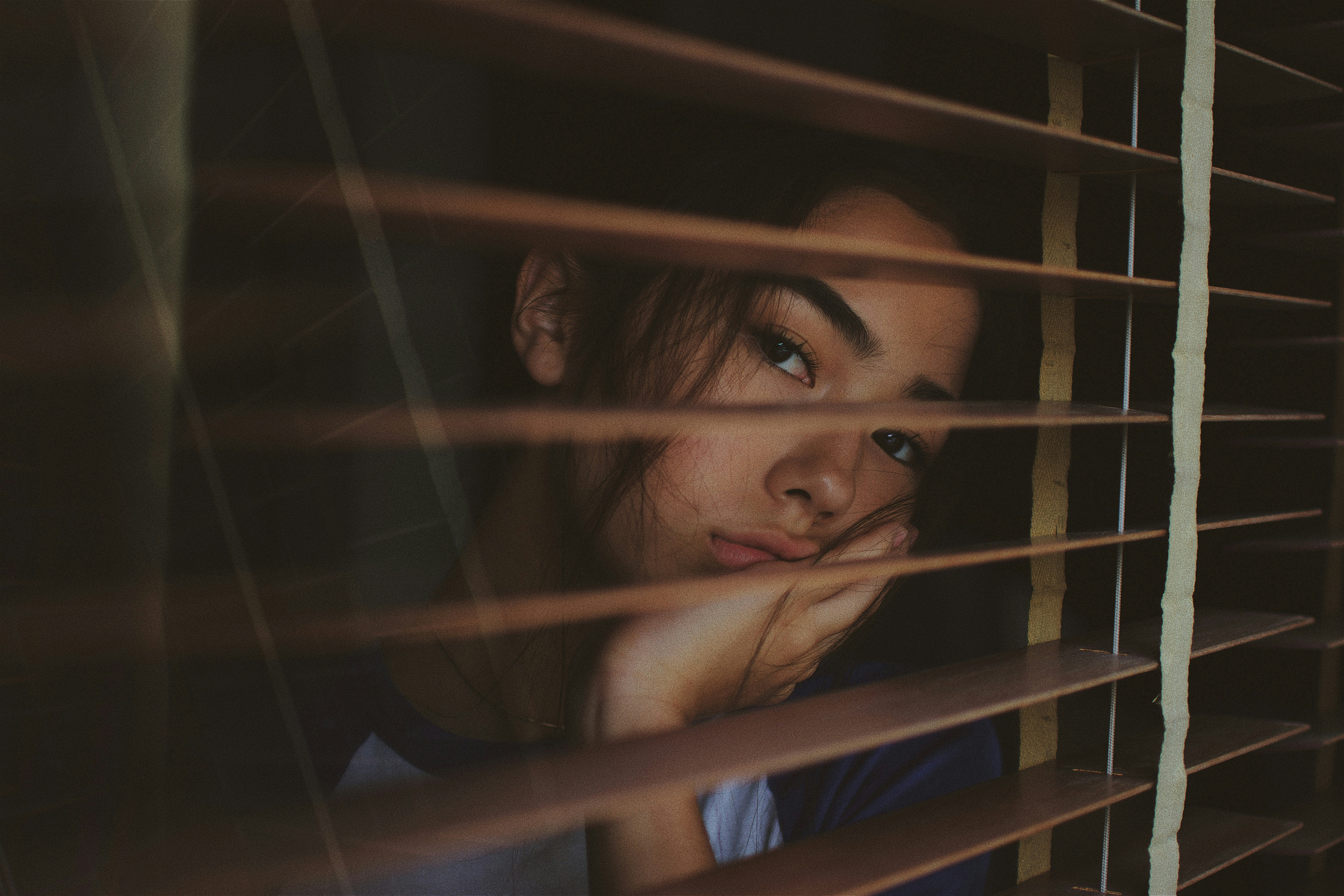 A female person sits sadly behind a window pane and gazes out of the window in depression / www.gastro-label.com